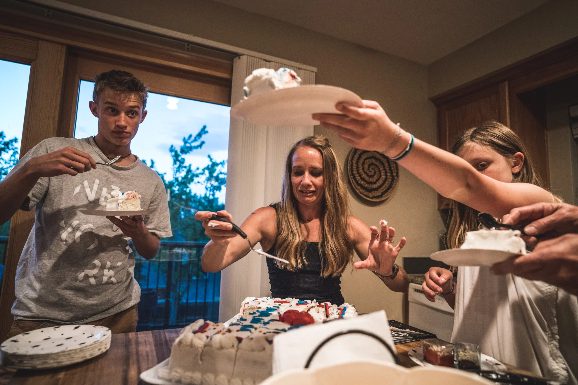 Color photo of a family in their kitchen eating graduation cake. Taken during their documentary event photography session in Denver, Colorado.