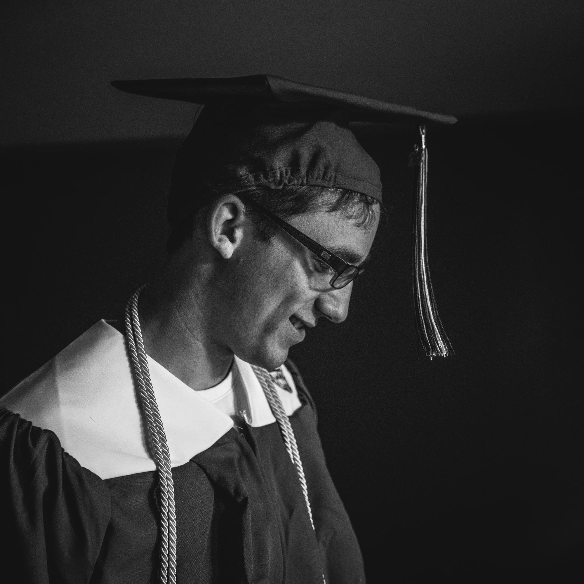 Black and white close-up photo of a young man wearing his cap and gown during a photography shoot documenting his graduation from Cherry Creek High School in Denver, Colorado.