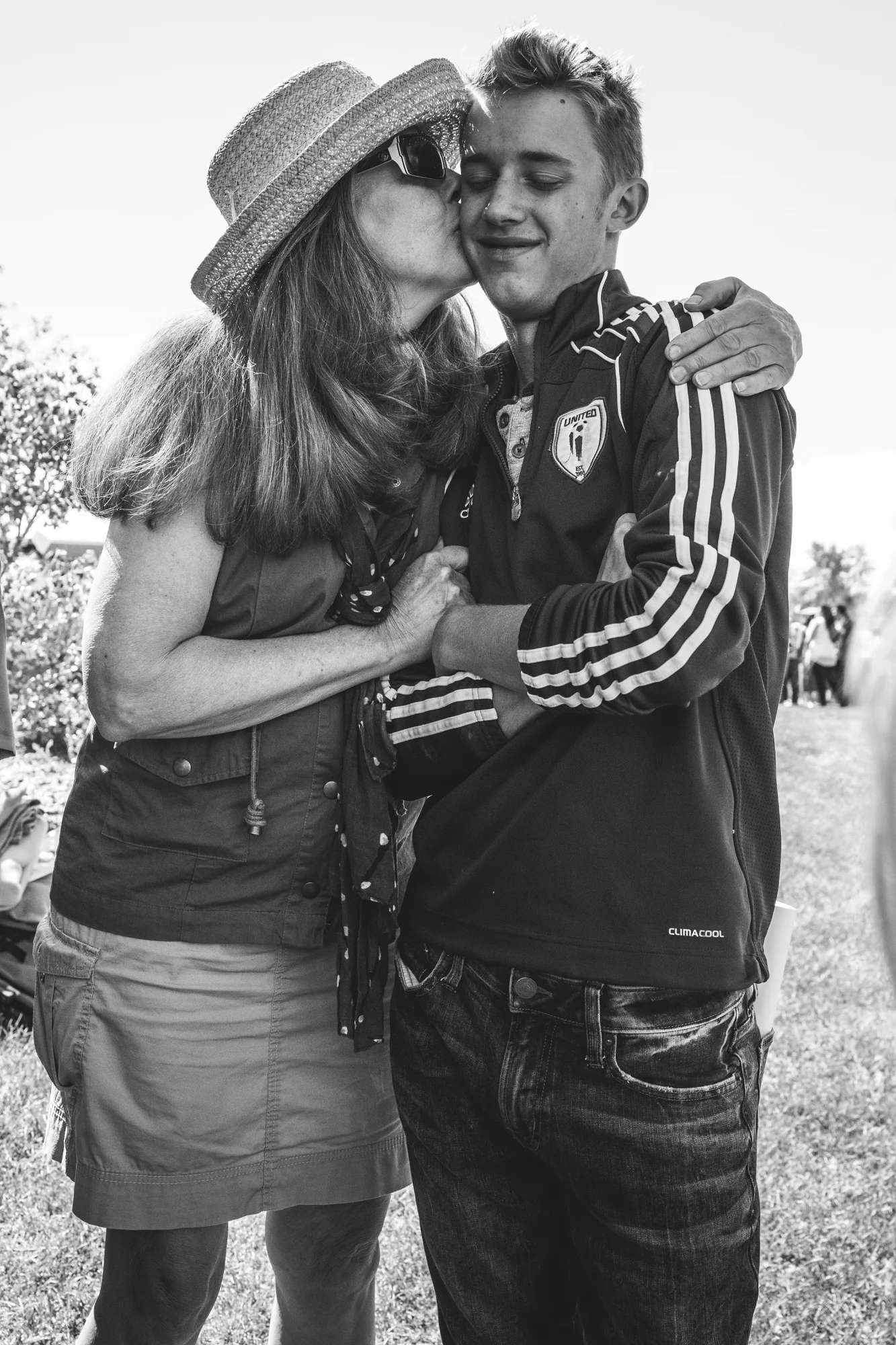 Black and white photo of a grandmother kissing her teenage grandson on the cheek. Denver, CO