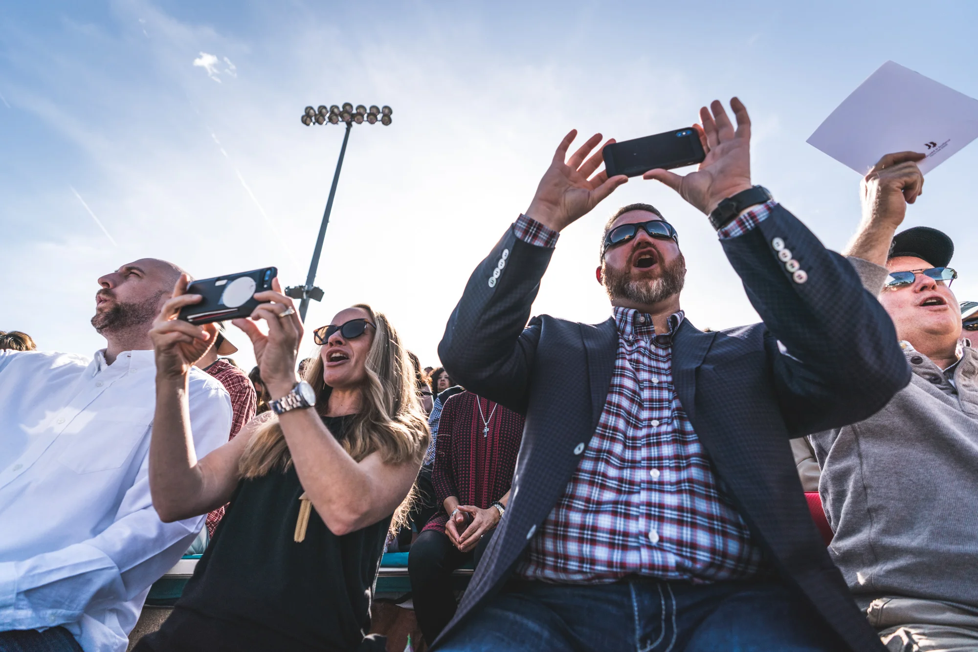 Color photo of a family sitting in bleachers, screaming for their son as he walks across the graduation stage. Taken at Cherry Creek High School in Denver, Colorado.