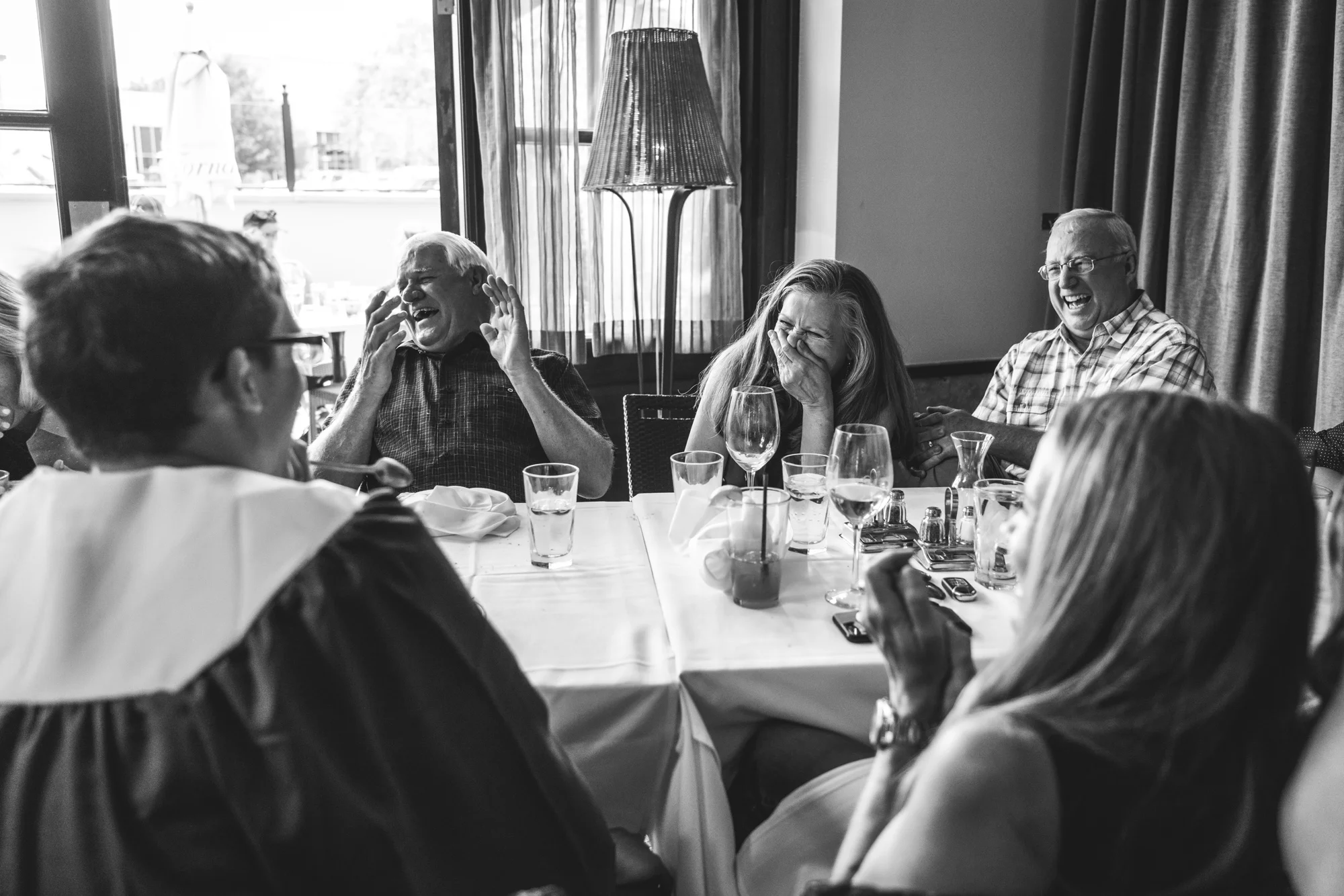 Black and white photo of a family laughing hysterically together while sitting at a table in a restaurant in Denver, CO.