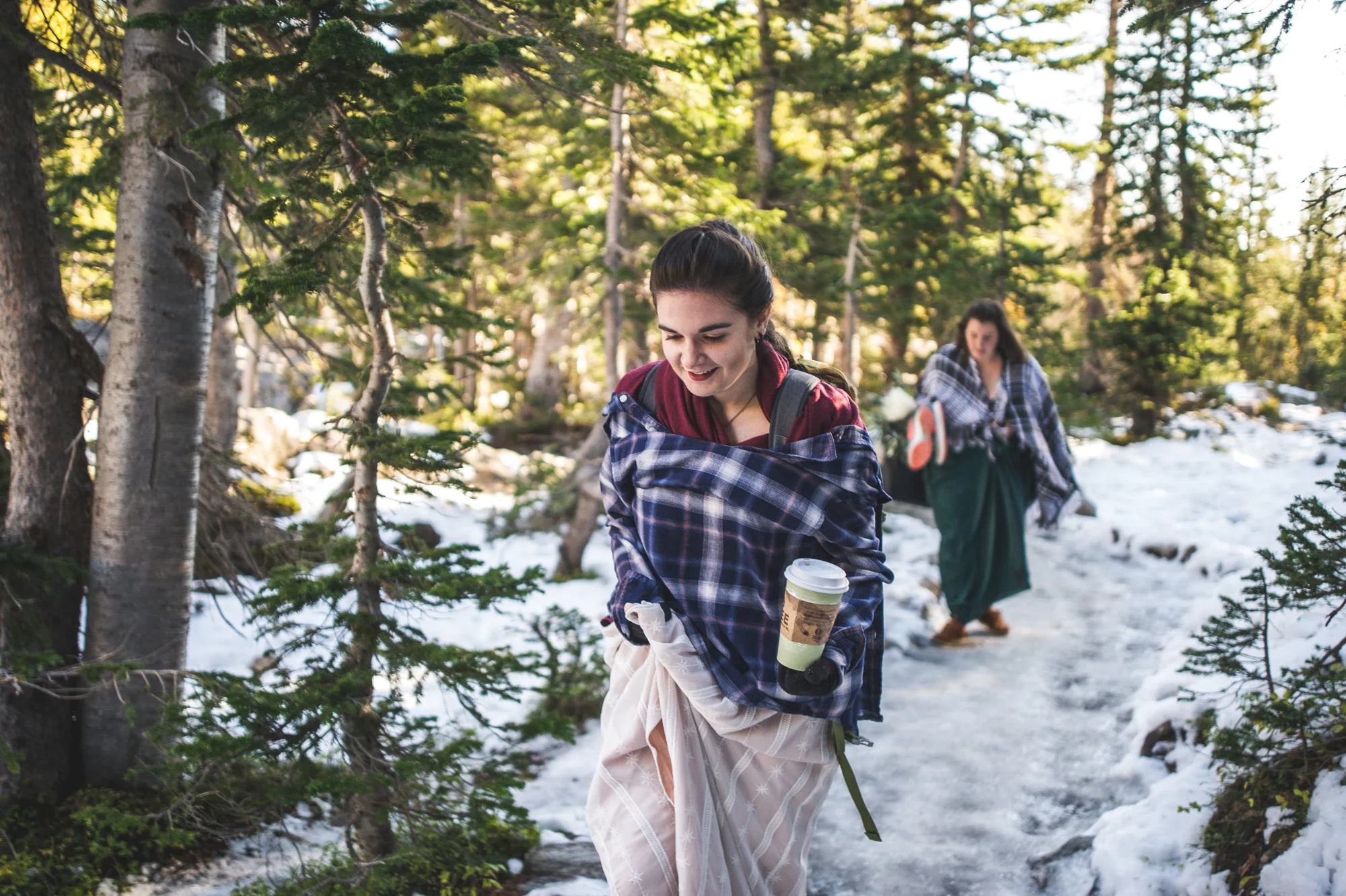 Color photo of a bride and her maid of honor walking in the Rocky Mountains with snow covered ground in their ceremony dresses