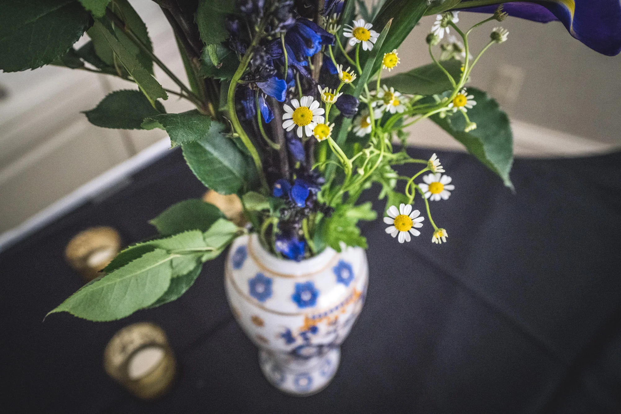 Tiny white flowers with yellow middles as well as blue irises rest in a white and blue vase on a table at a wedding reception