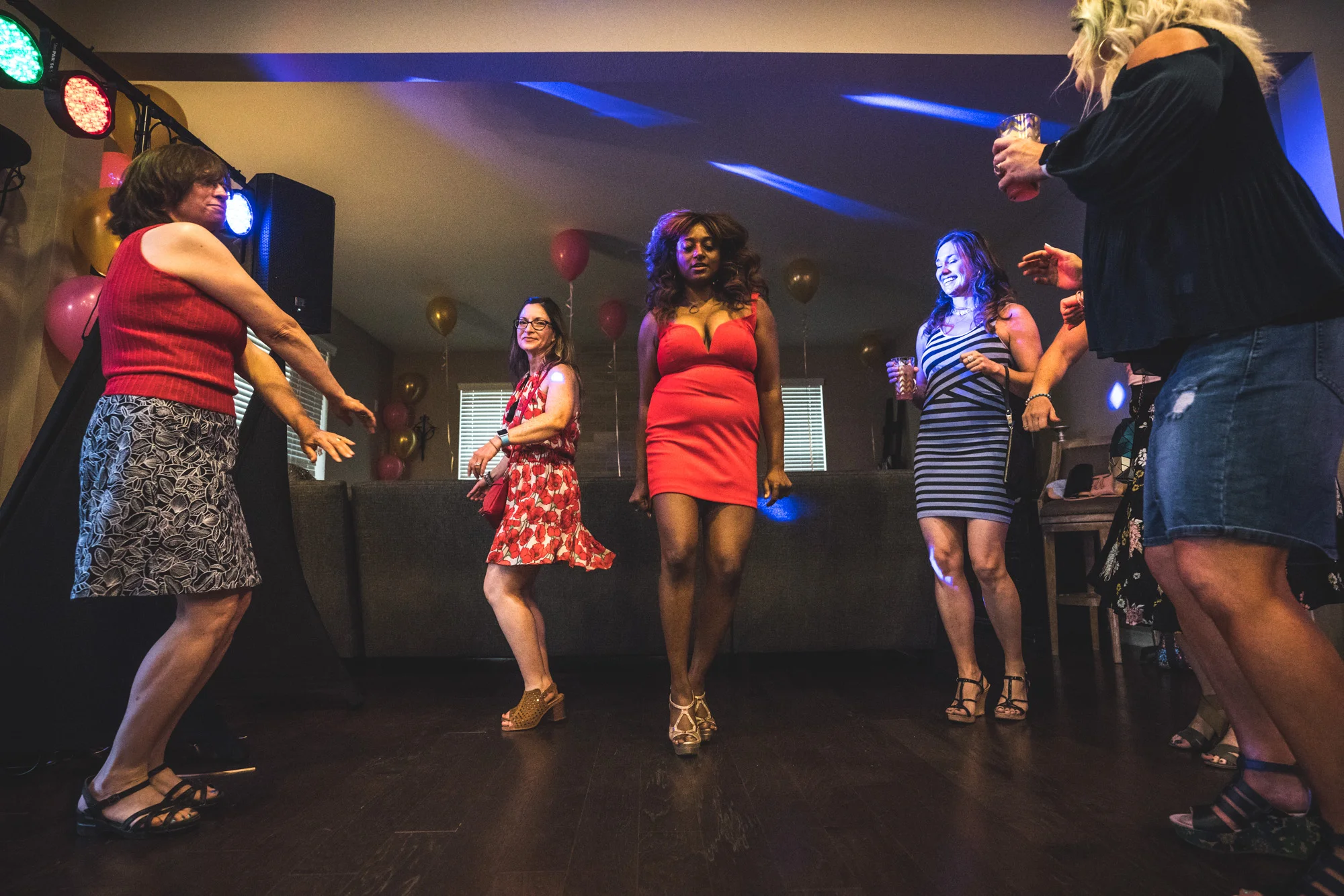 Documentary photography image of a woman at her birthday party at her home, dancing in the living room surrounded by brightly colored lights and balloons