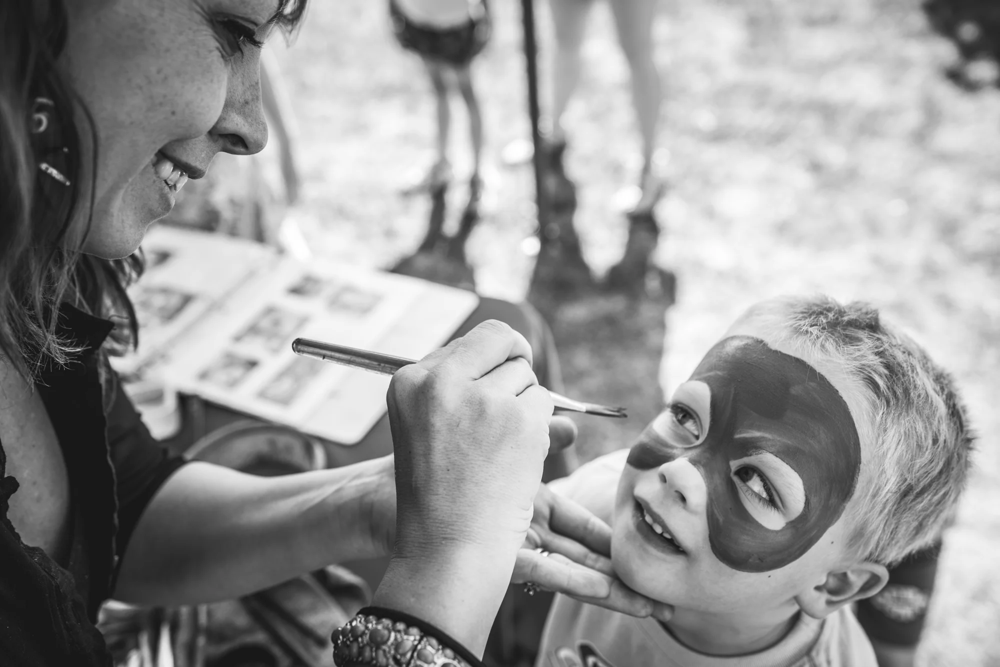 Black and white photograph of a little boy getting his face painted at an outside fundraising event in Denver, Colorado