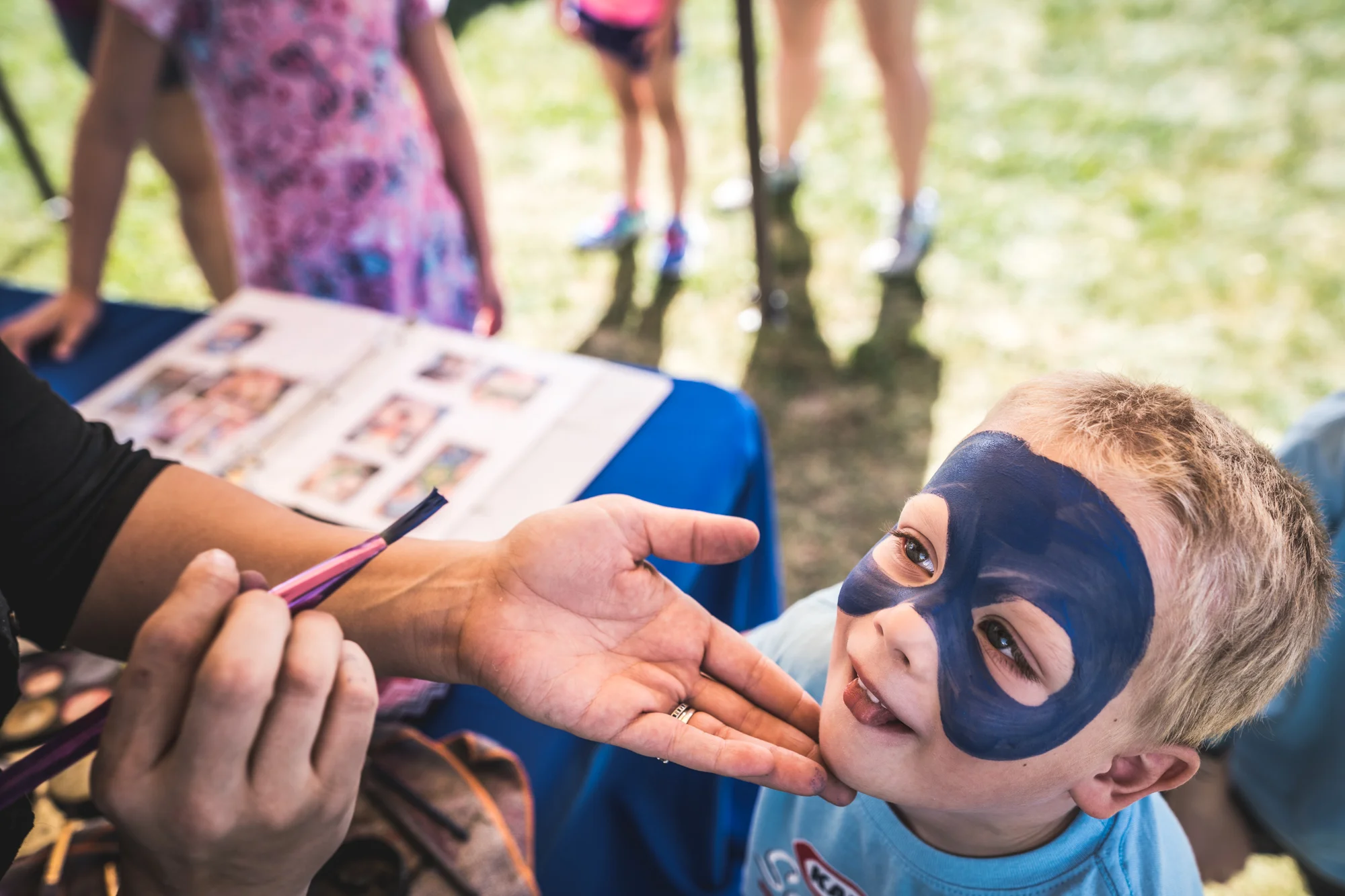 Color photo of a little boy getting his face painted blue at a charity event in Denver, Colorado