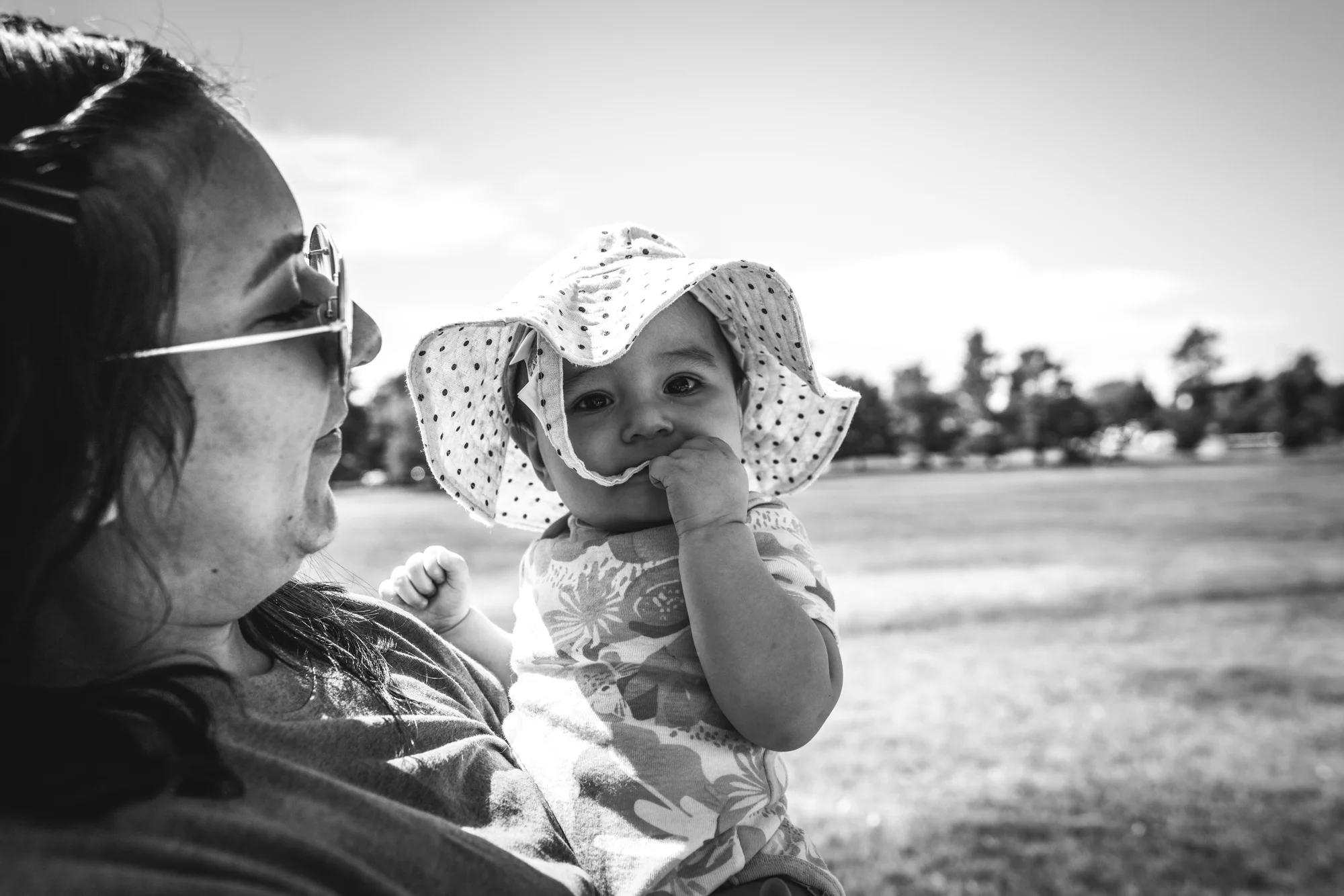 black and white image of a mother on a walk while holding her sweet baby girl who is wearind a white polka dotted hat