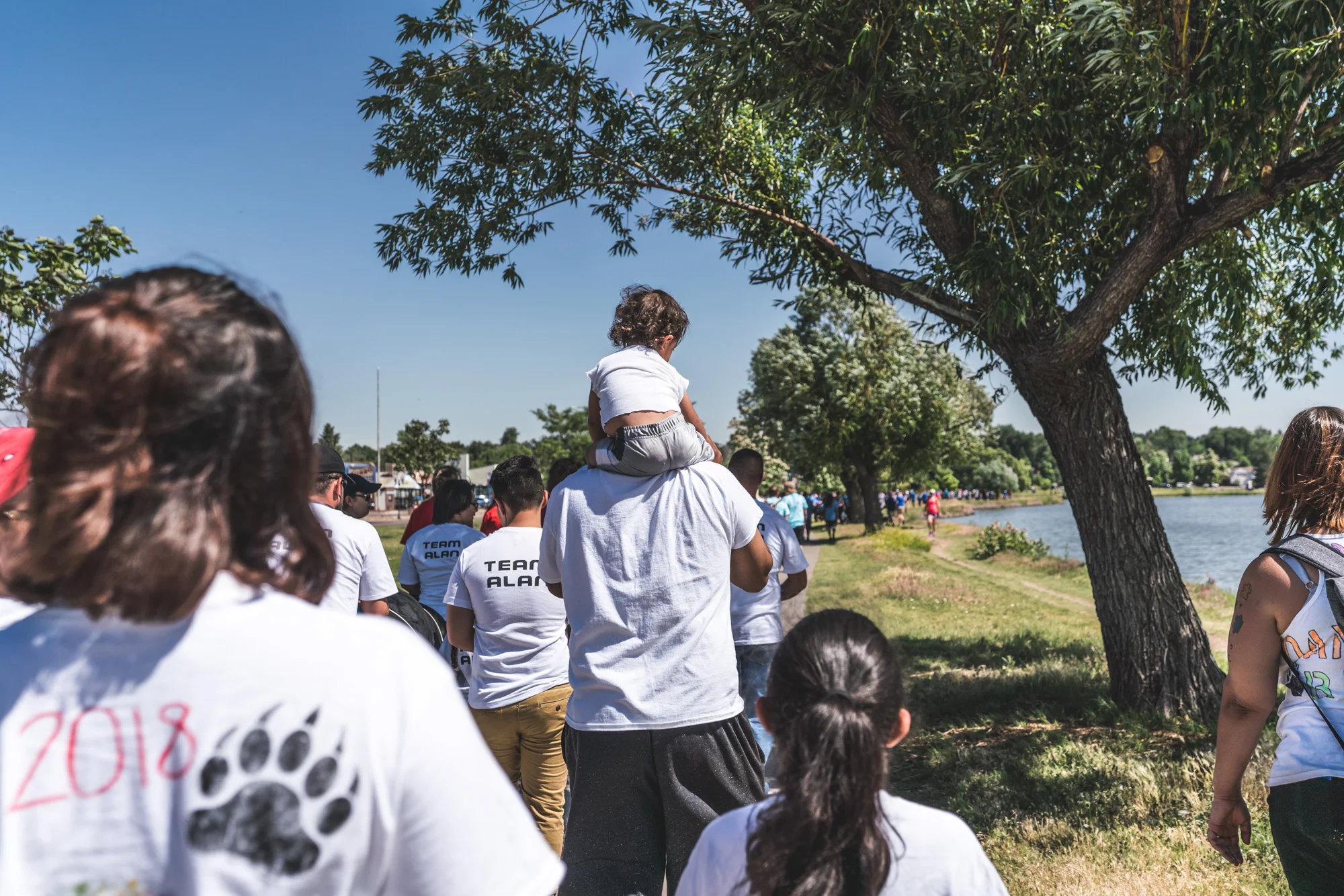 Group walks around Sloan's Lake in Denver for the Autism Society's Walk with Autism event, a little girl on her father's shoulders