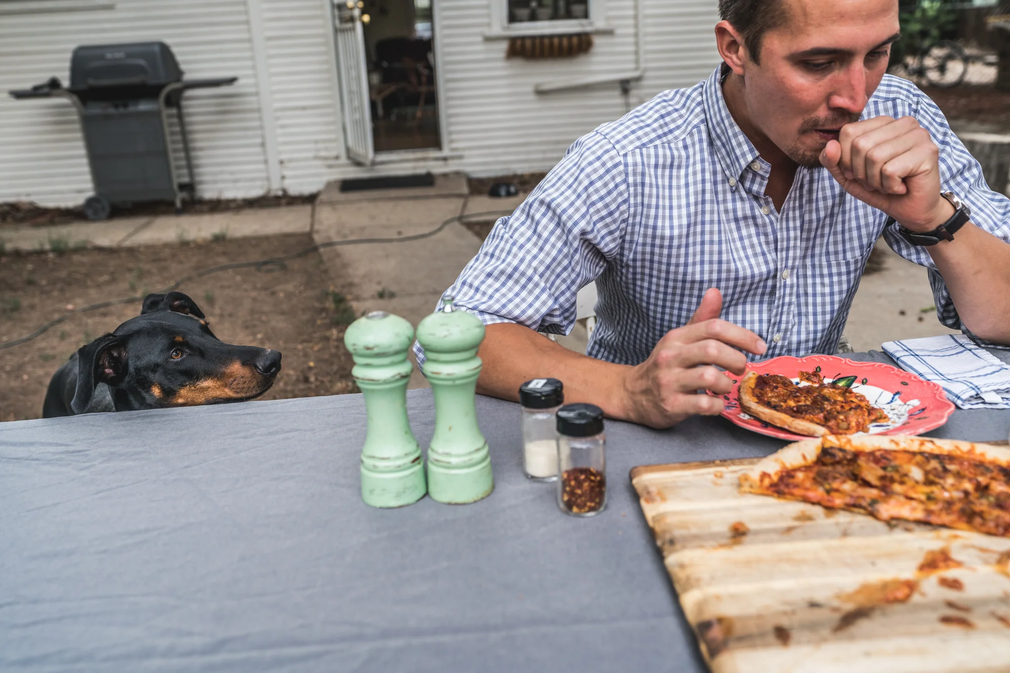 Man sitting at an outside table coughs after eating spicy pizza as his dog watches on