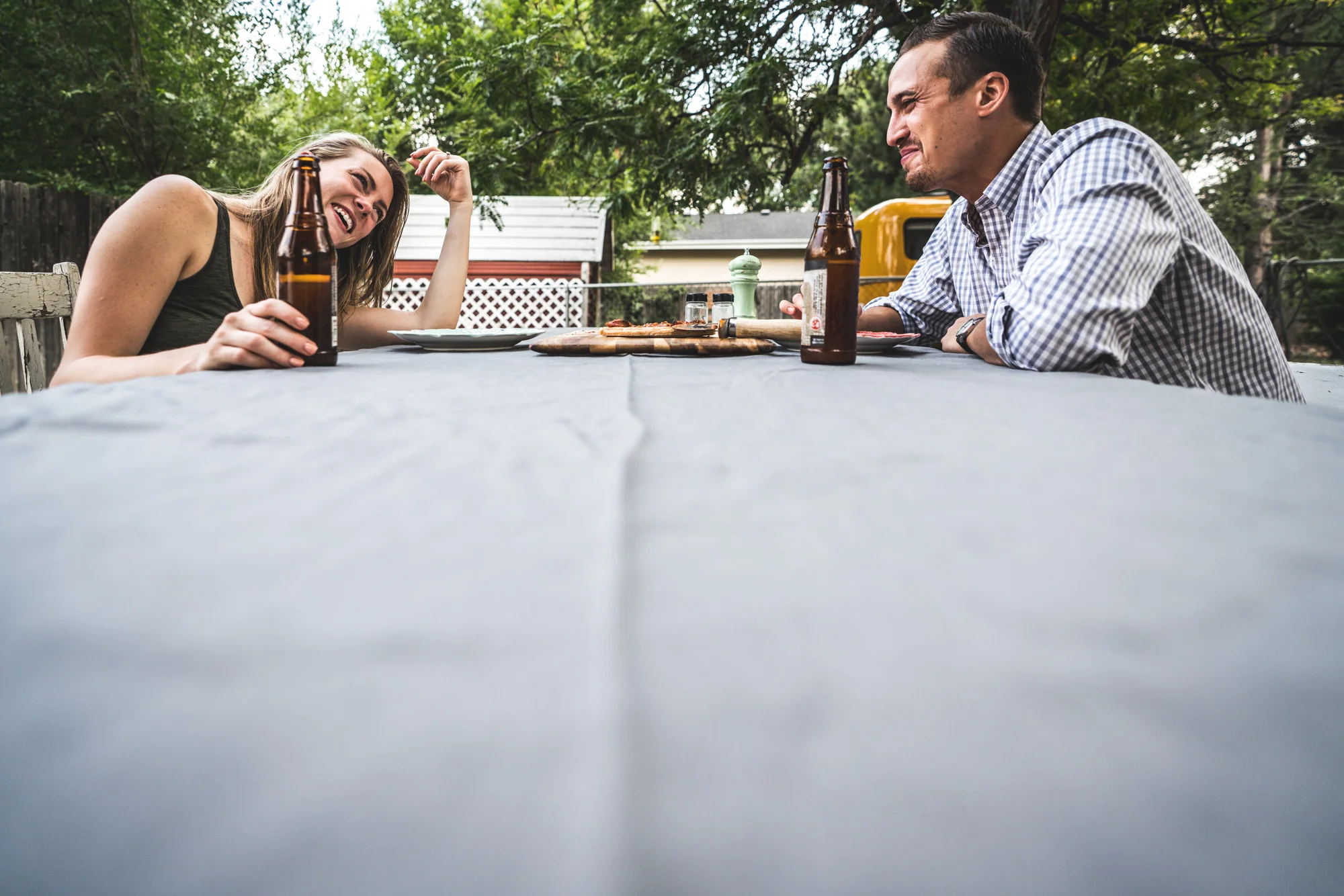 Man and woman drinking beer at an outside table laugh and smile at each other