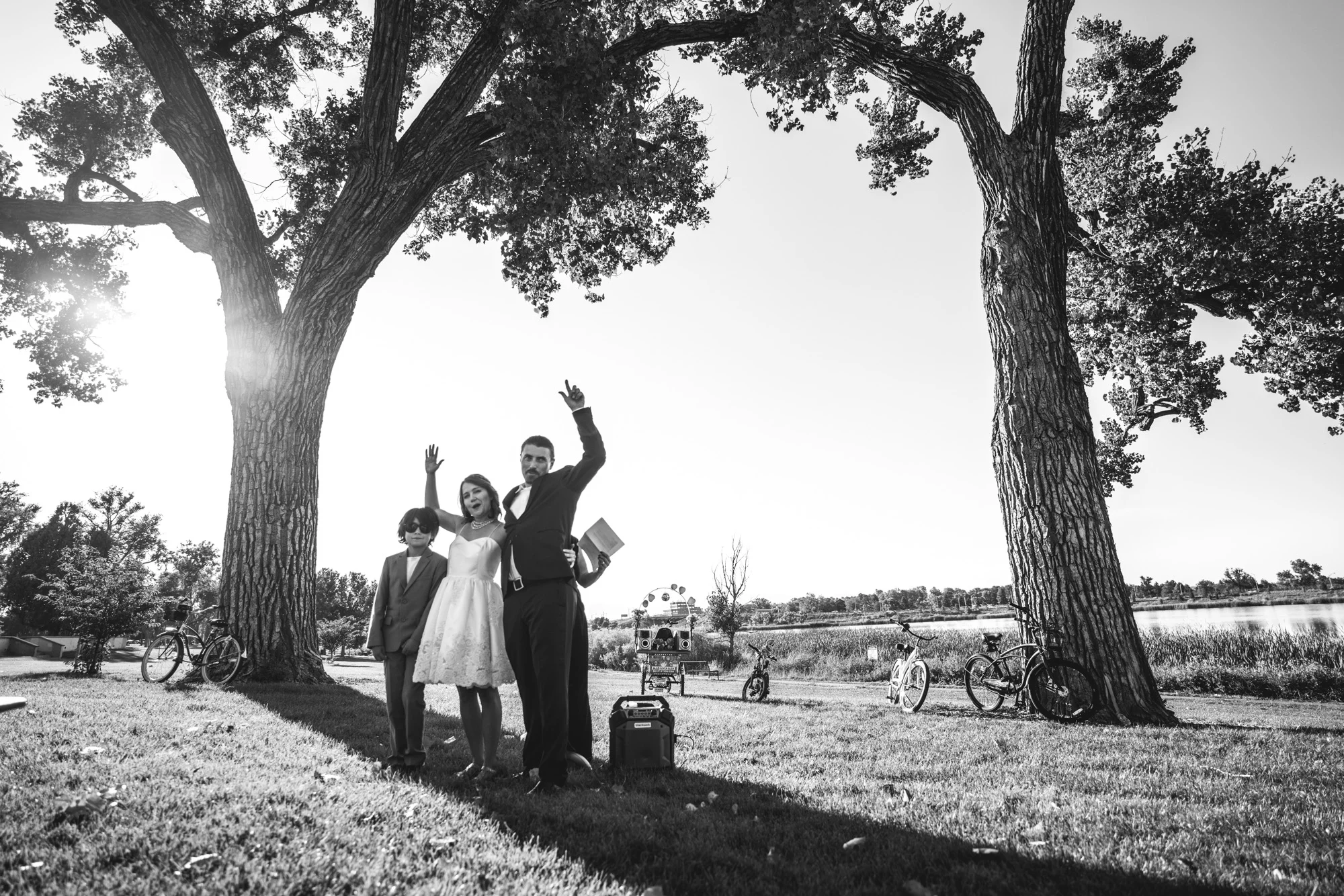 Newlyweds and groom’s son stand under a tree, arms up in celebration