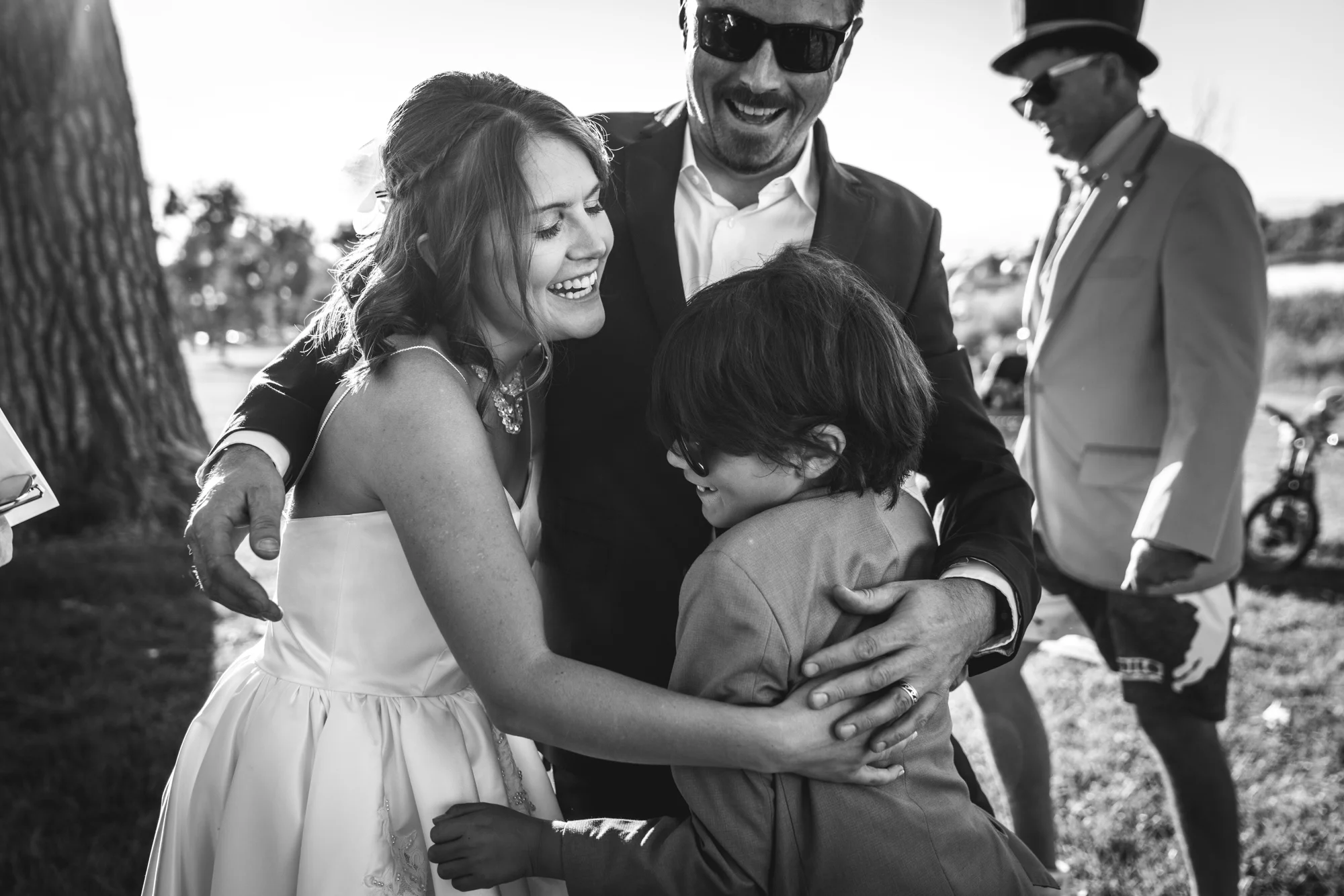 Bride, groom, and groom’s young son give each other a big hug and smile in celebration of bride and groom getting married