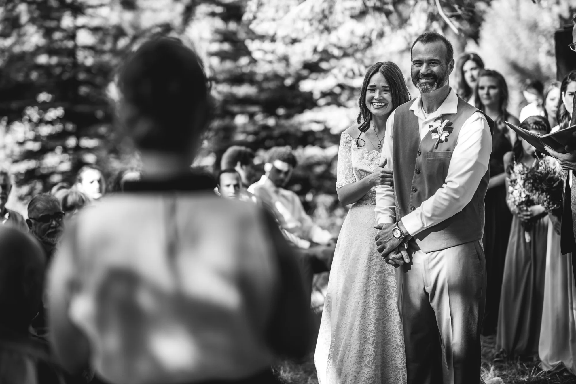 Bride and groom smile wide as a family friend reads a speech during their wedding ceremony