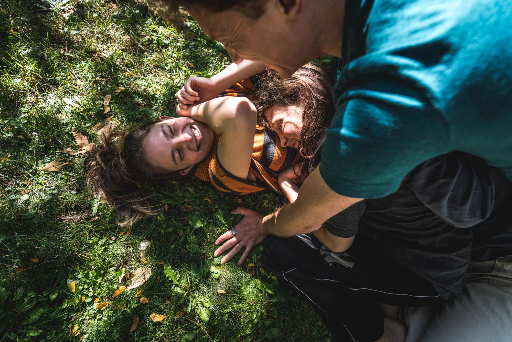 Dad and two kids dogpile and smile in the grass in their yard