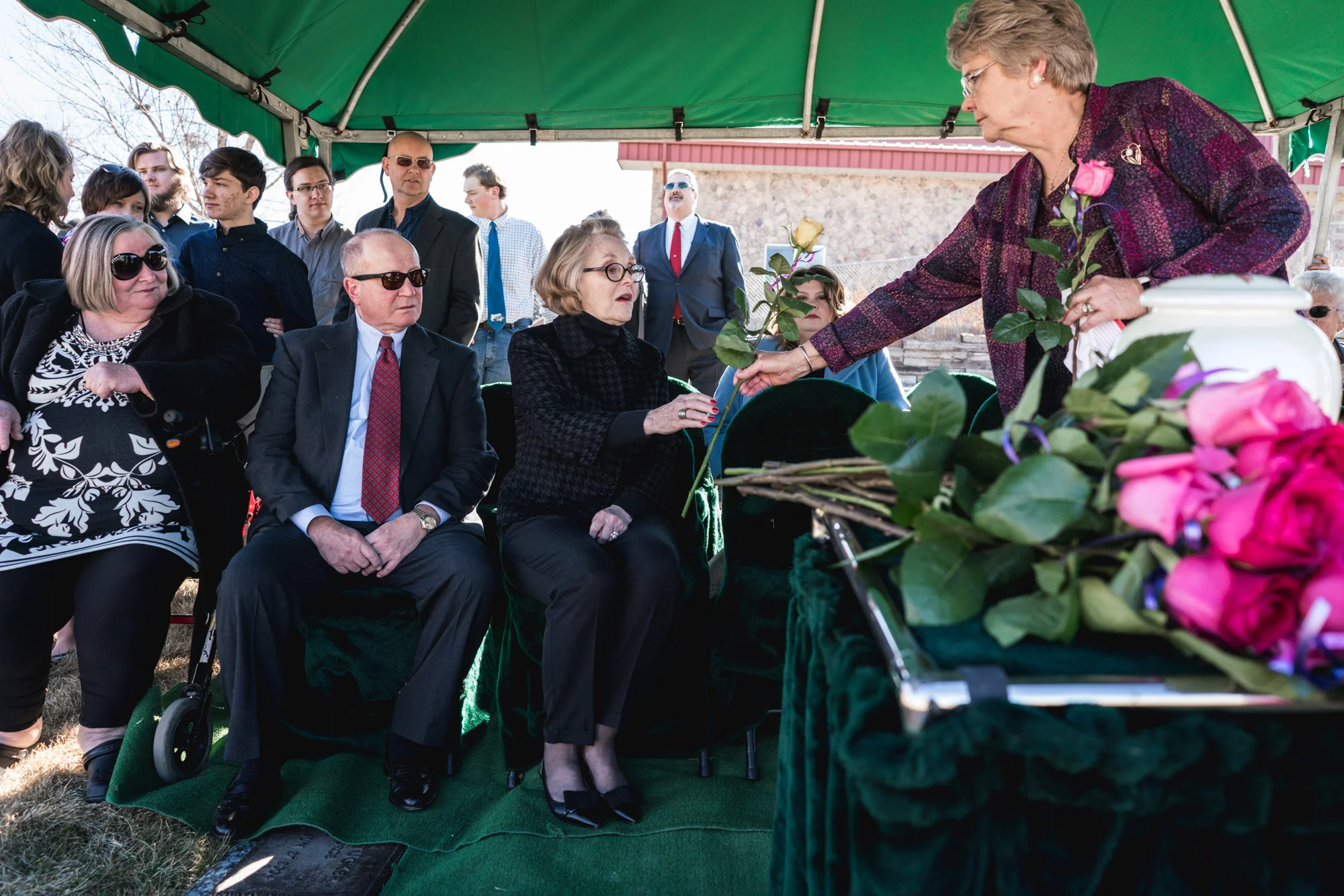 A woman hands another a rose during the memorial service of a lost loved one under a tent at a cemetery in Greeley, Colorado