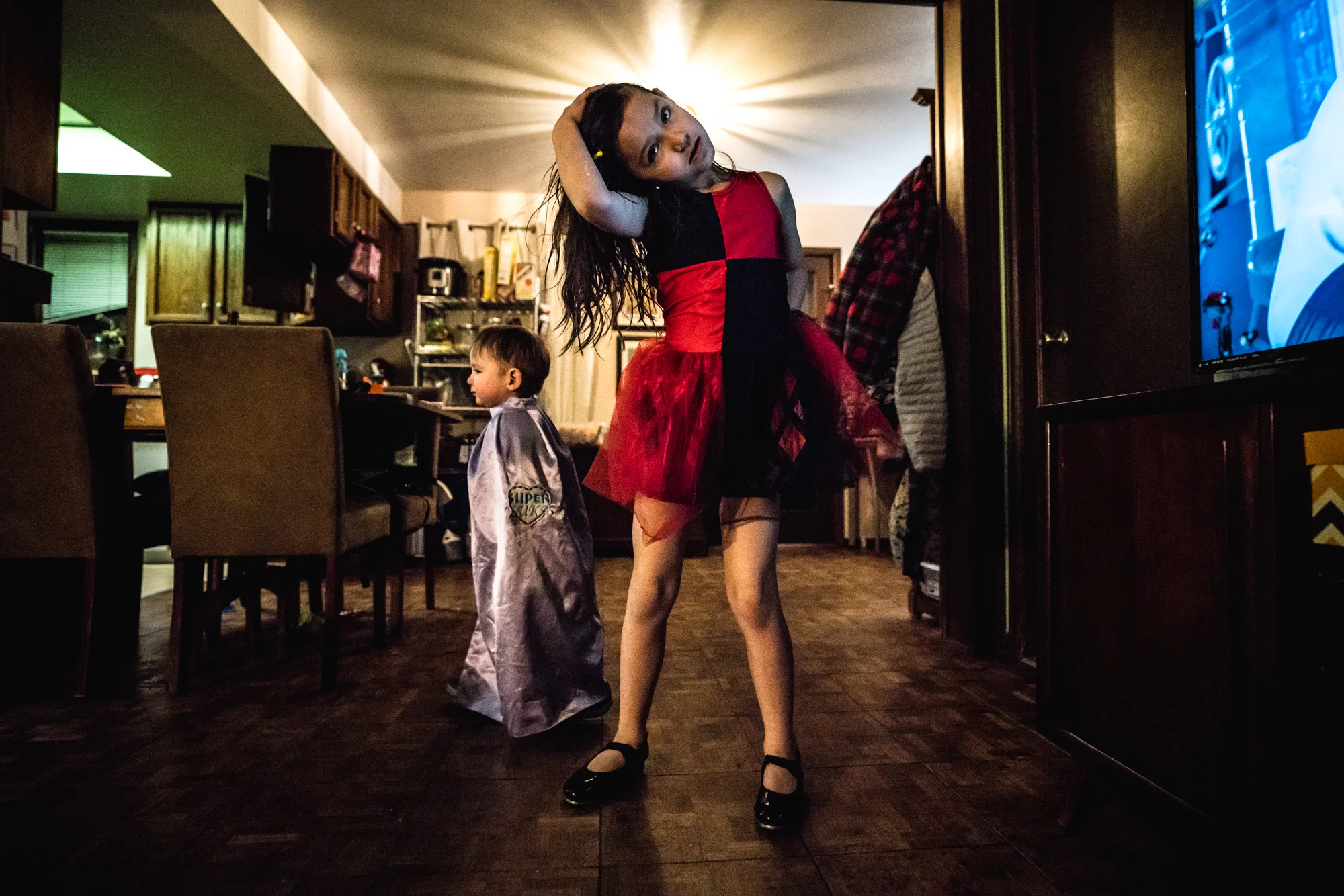 Two children wearing Halloween costumes in their living room at home, with the little girl looking straight to camera