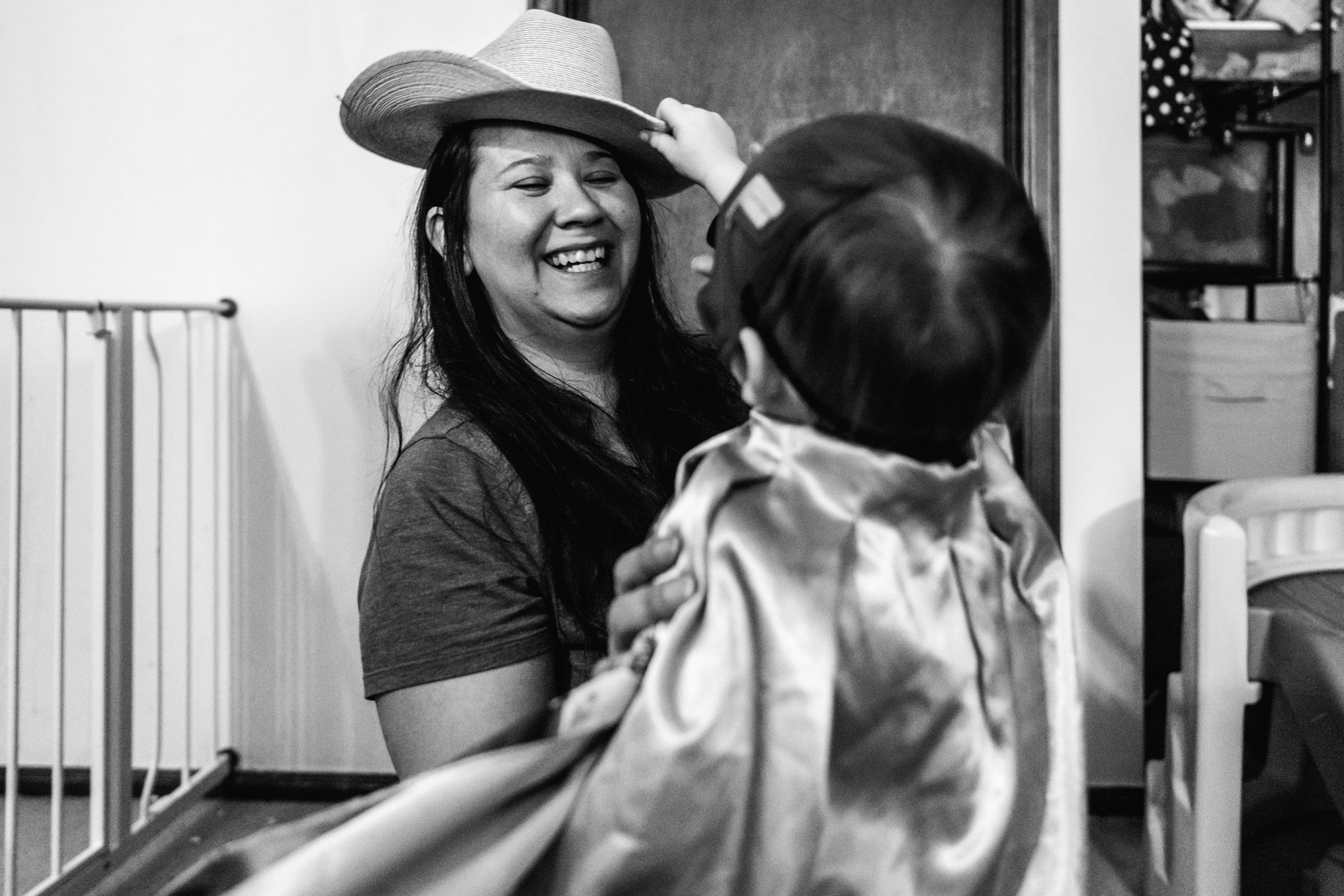 Little boy wearing a cape tries to steal his mom’s cowboy hat