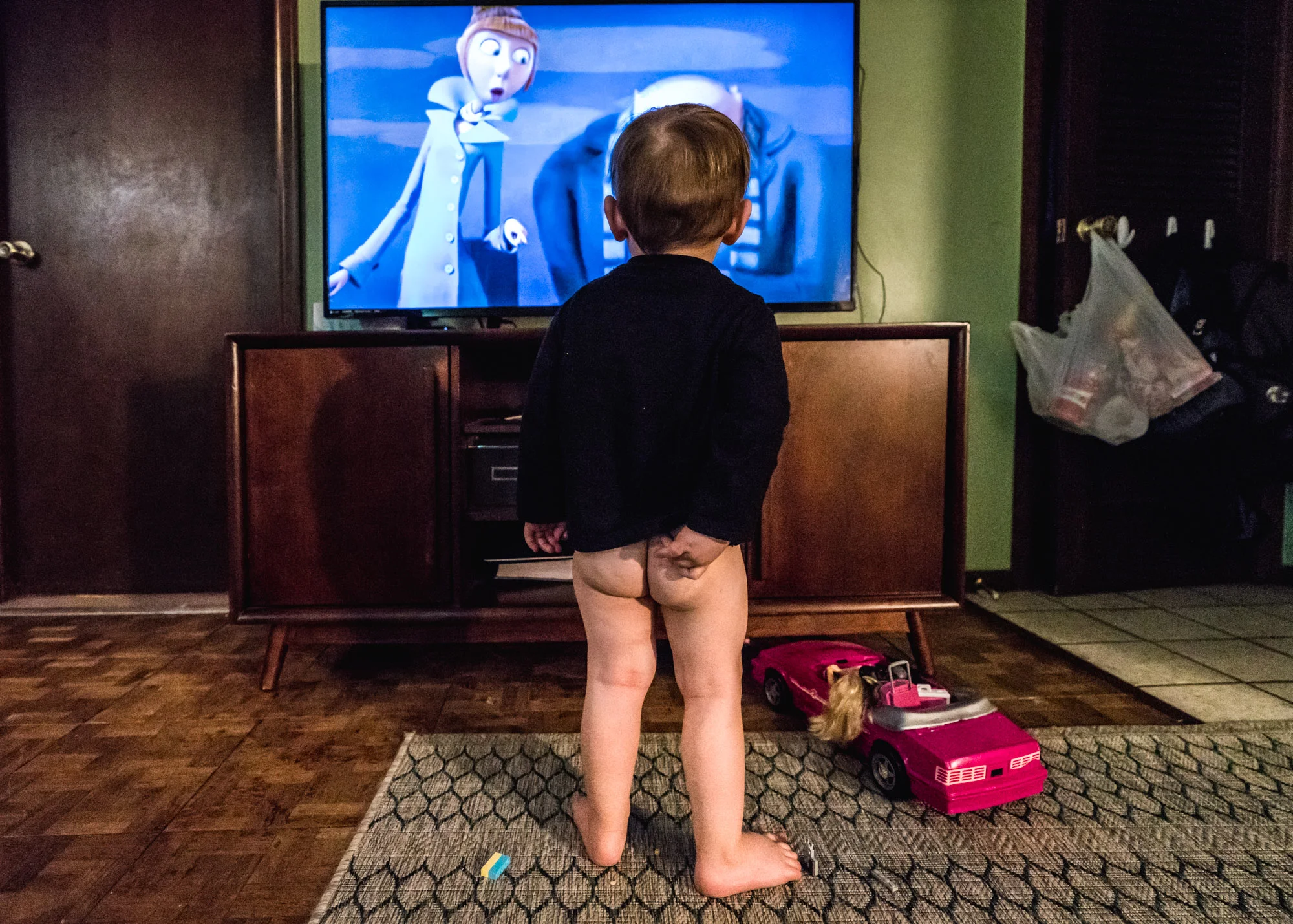 Little boy with no pants on watches television as one of the characters on the movie looks over with shocked eyes, as if she’s shocked at seeing the naked little boy.