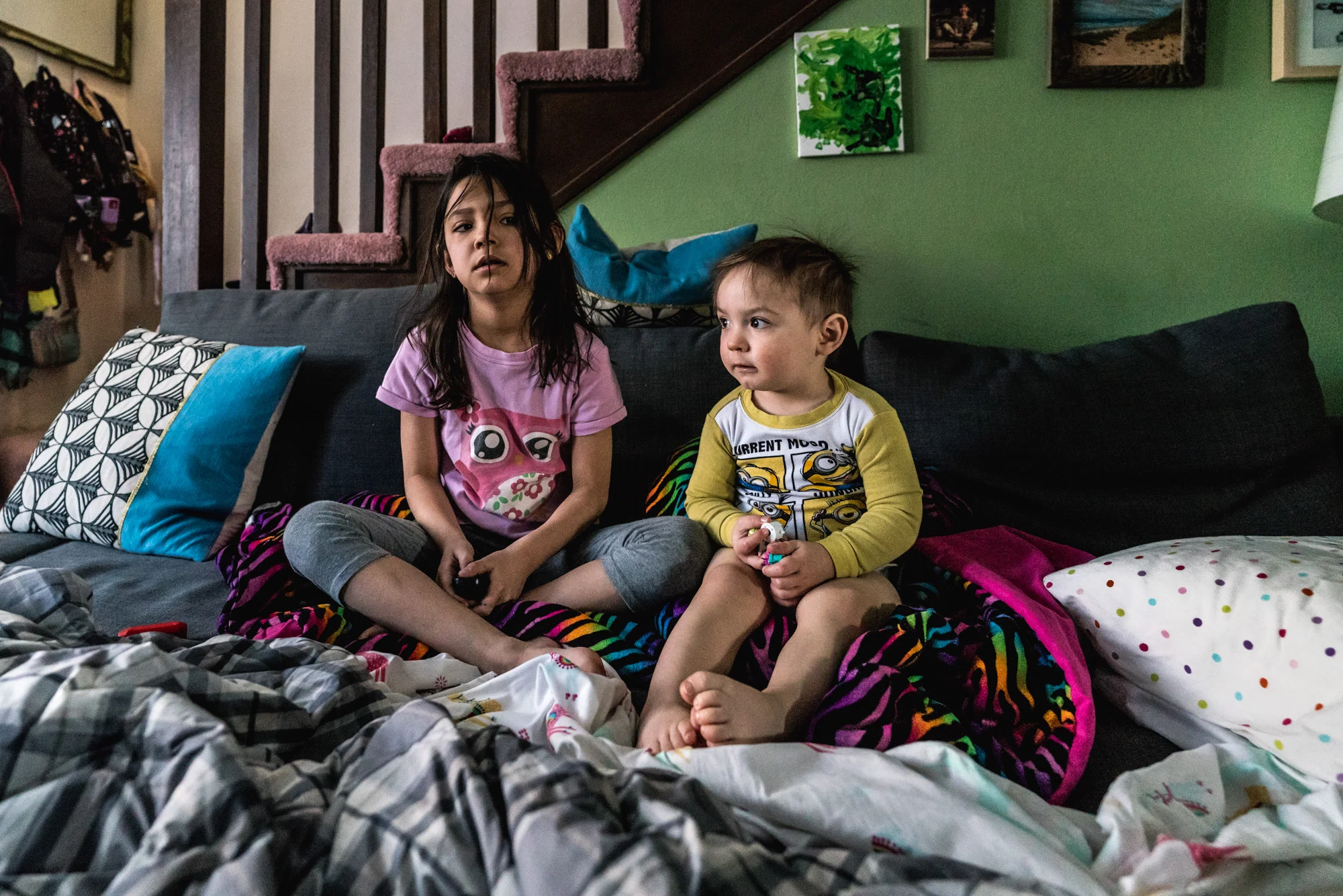 Little boy and little girl in their pajamas sitting on a couch bed downstairs in the early morning, looking as if they were still tired