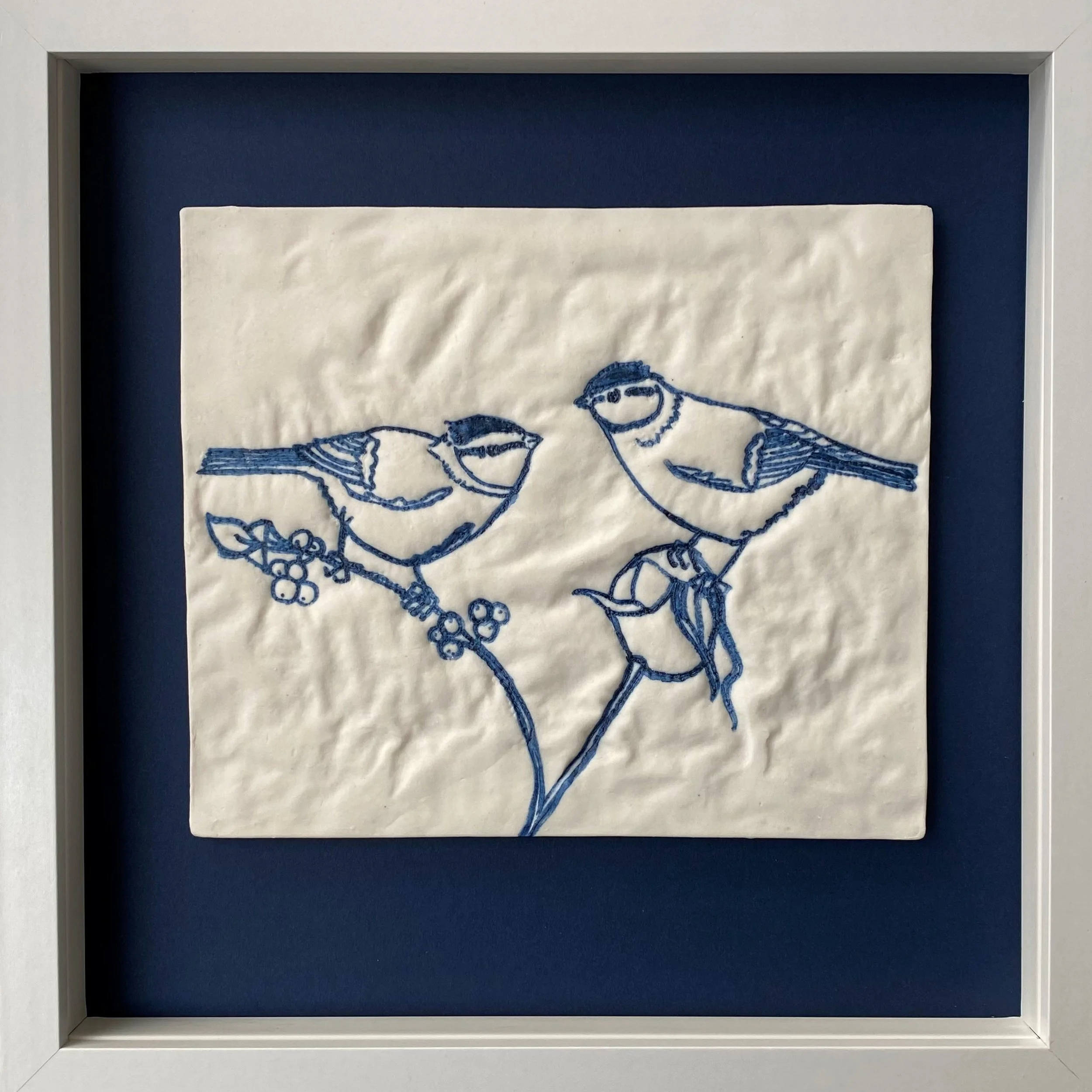  embroidered artwork of two birds perched on a branch, framed and displayed on a wall
