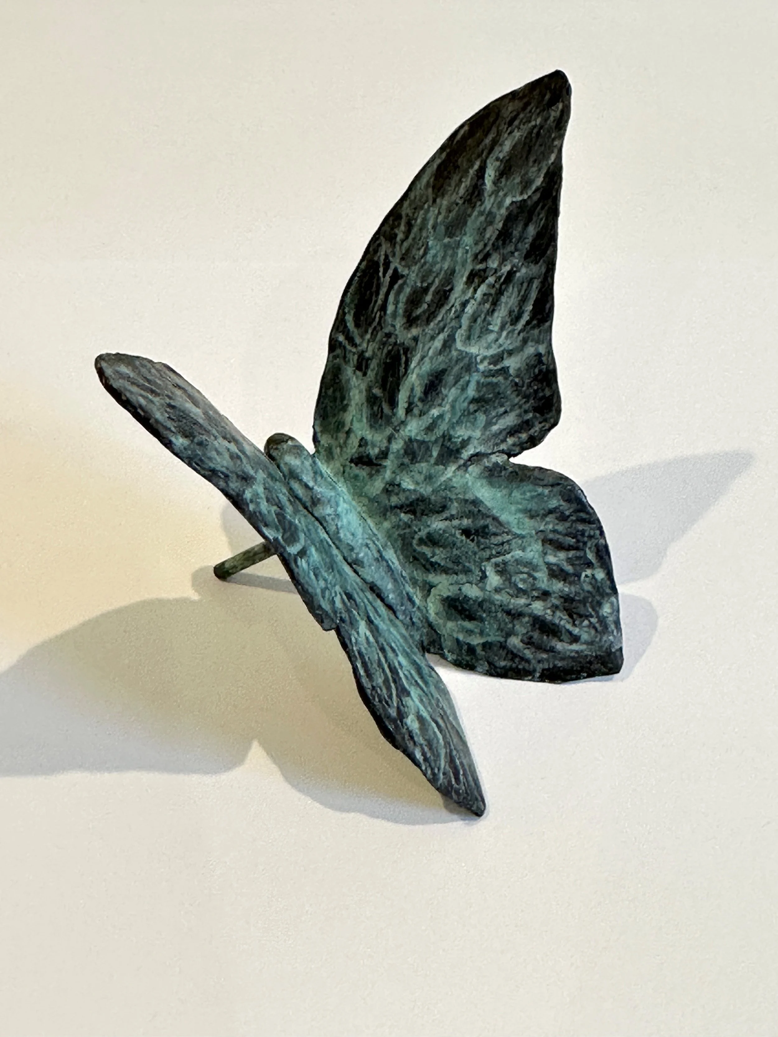 A metallic butterfly sculpture with brown and blueish wings on a light background.