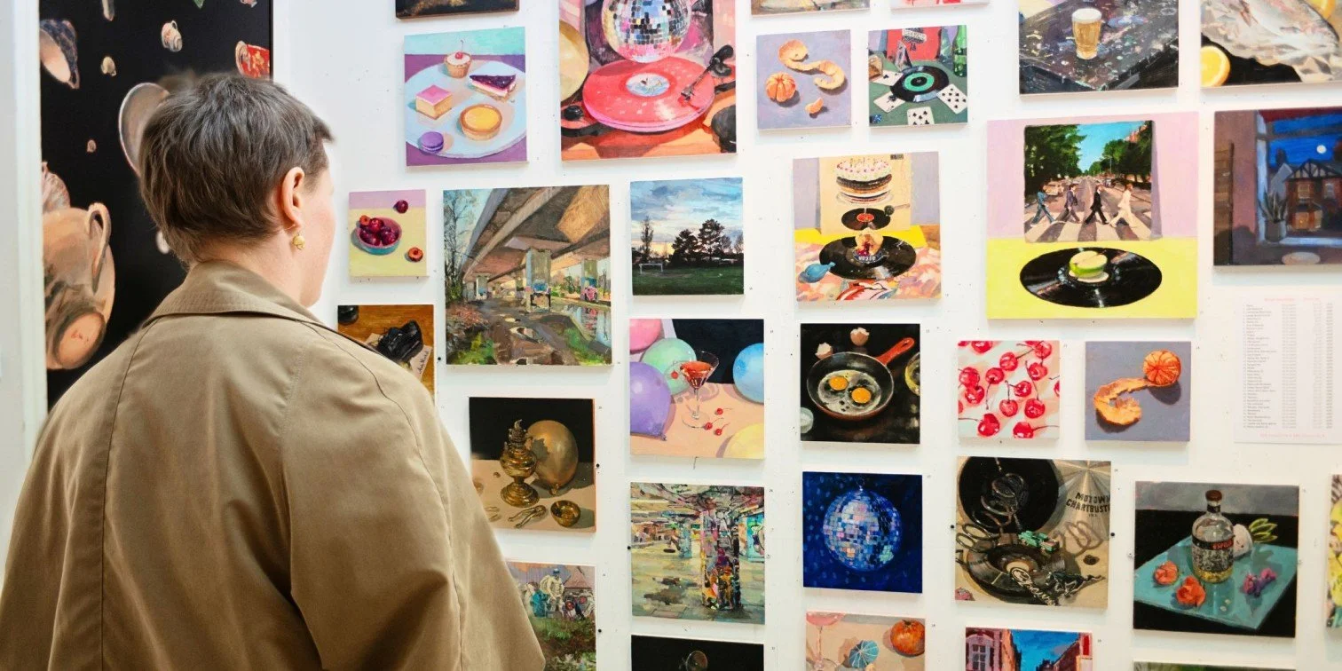 Art show visitor staring at several paintings hanging on the wall inside of an art studio.