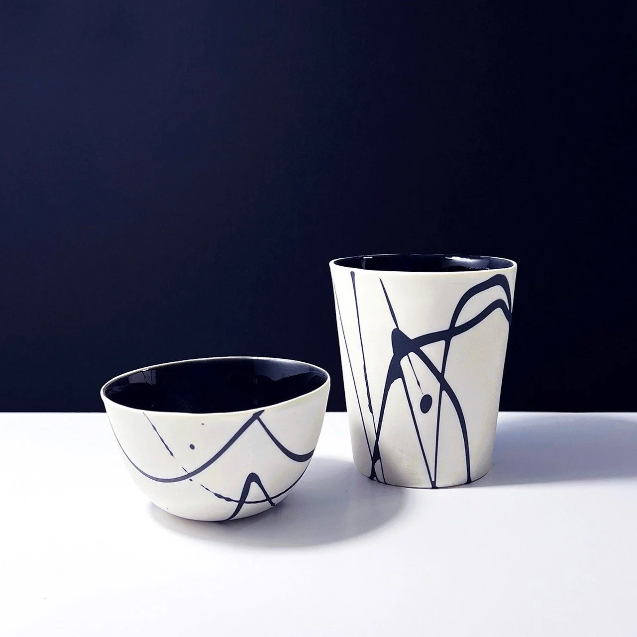 A white ceramic vase with light blue floral pattern, gold rim, placed on a white surface against a dark background.