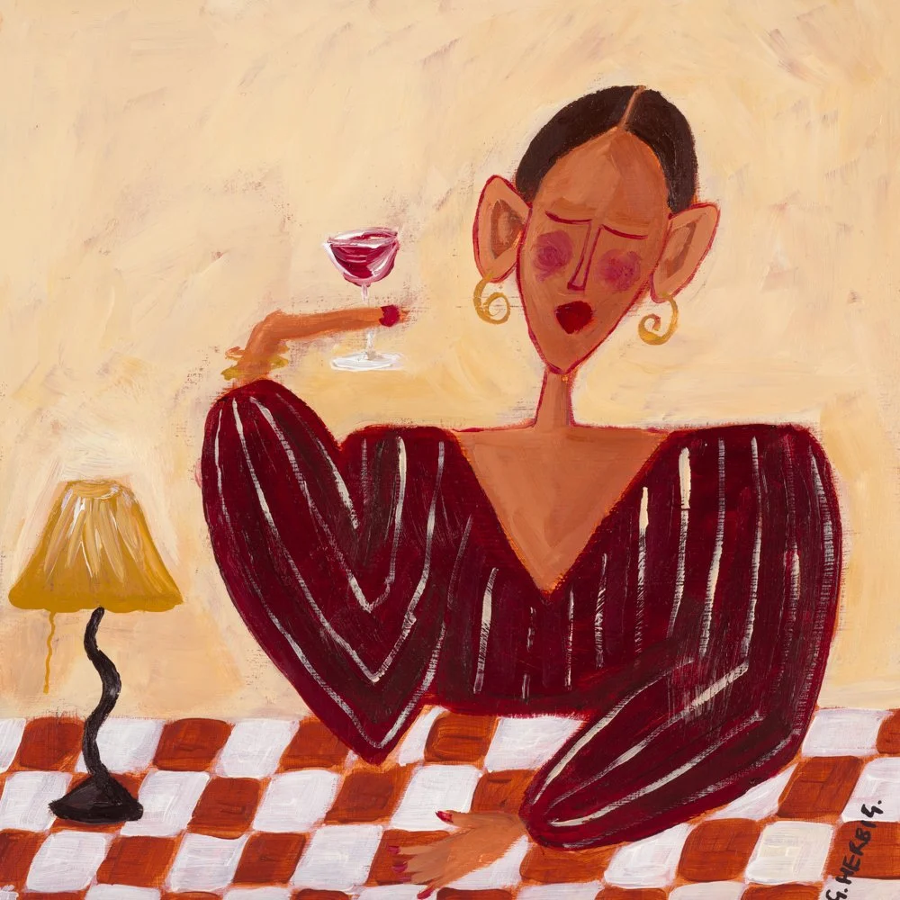 A woman with large earrings and makeup, sitting on a checkered tablecloth, reading a book with a glass of wine nearby, and two lit candles on a candle holder.