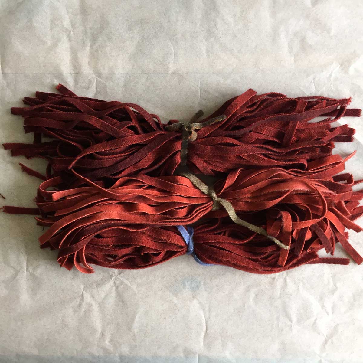 bundles of dark red wool strips for making a hooked rug