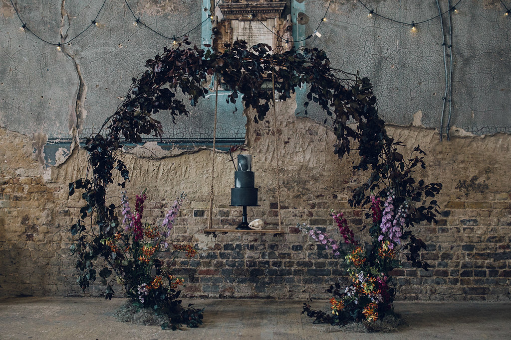 Black wedding cake on a floral cake arch swing - Asylum Chapel Wedding, London 