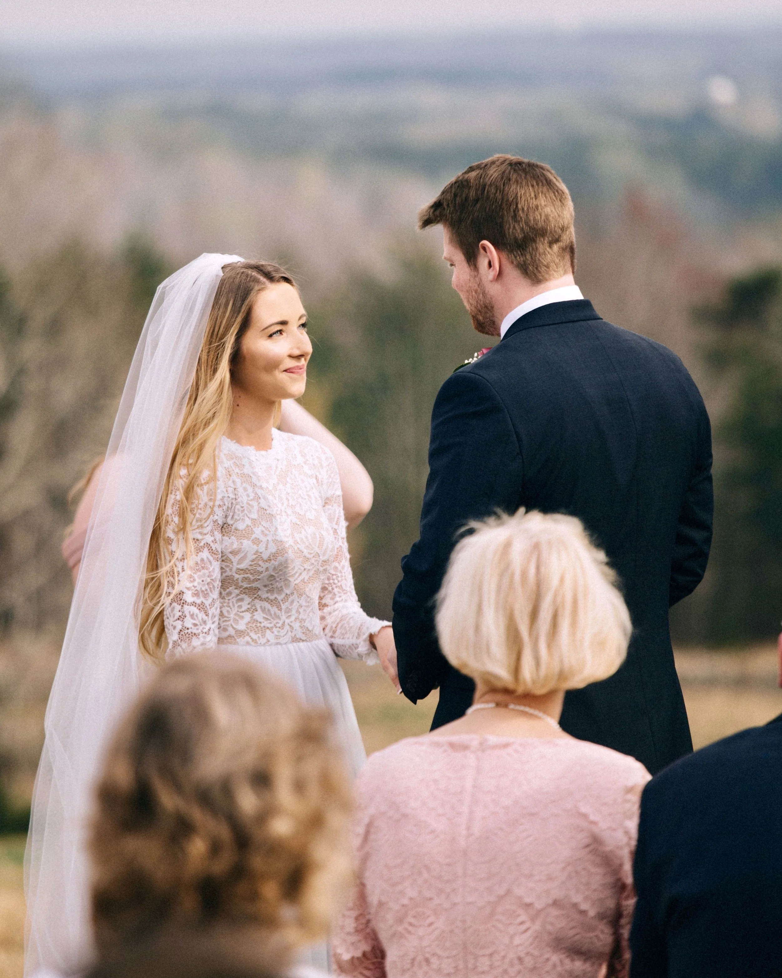 A bride and groom holding hands during an outdoor wedding ceremony, with guests watching.