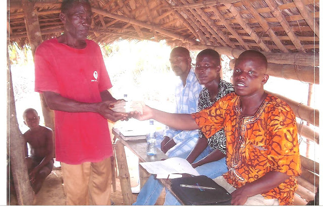 ere Emmanuel (in the orange shirt) is presenting David Bweh, the owner of the land, with the first check. (Also pictured are Emmanuel Sumo, the art teacher at the Vine School System of Christ, and Prince, a friend and member of the church)