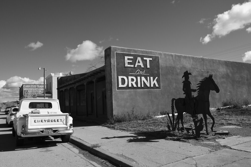 Painted "Eat and Drink" Sign on a Wall of a Now Closed Restaurant in Carrizozo With Cowboy Sculpture