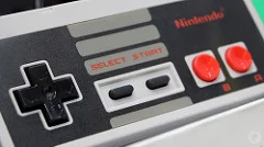 Image of the NES Classic Edition controller. It is rectangular, with the classic direction controller on the left, start and select in the middle, and A and B circle action buttons on the right.