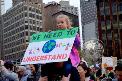 Little girl sitting on someone's shoulders at one of the March for Science events, holding a sign which reads, "We need to understand."