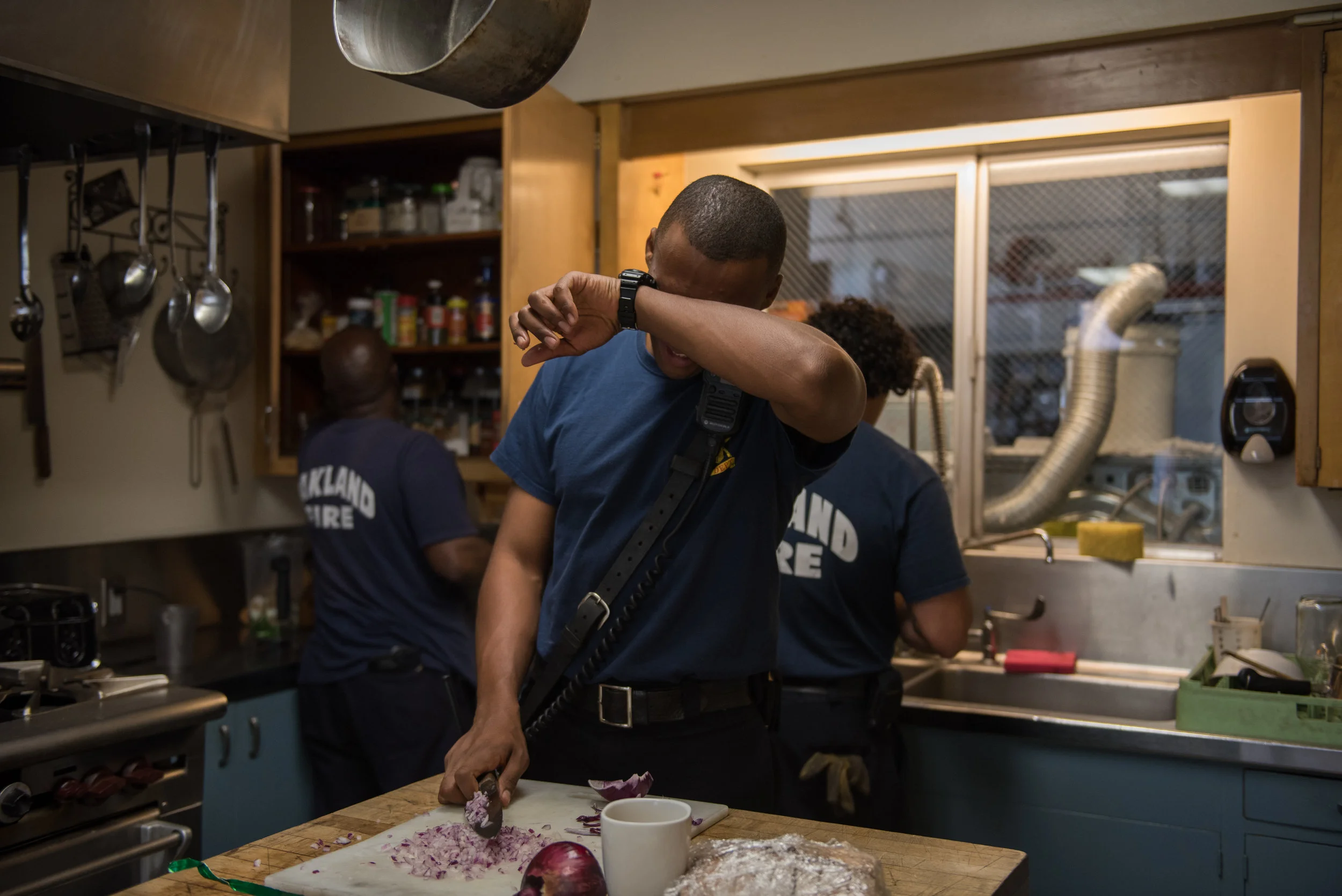 Firefighter Paul Mason Jr wipes his eyes as he chops onions for the crew’s dinner at Oakland’s Station 23 on Monday, June 26, 2017. | Rosa Furneaux for the East Bay Express