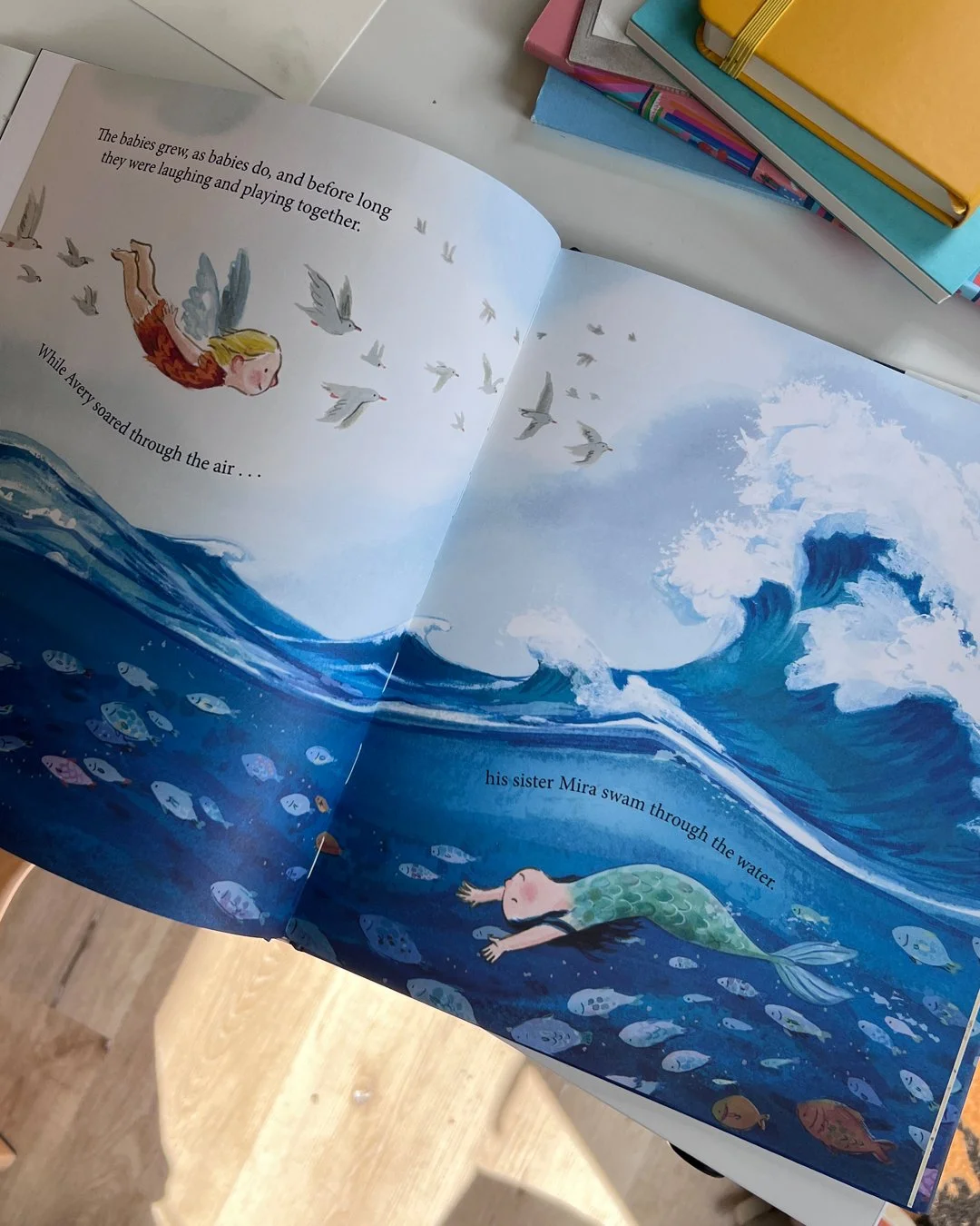 an open book with full bleed illustration of waves. An angel flies in the air and a mermaid swims in the sea with the fish.