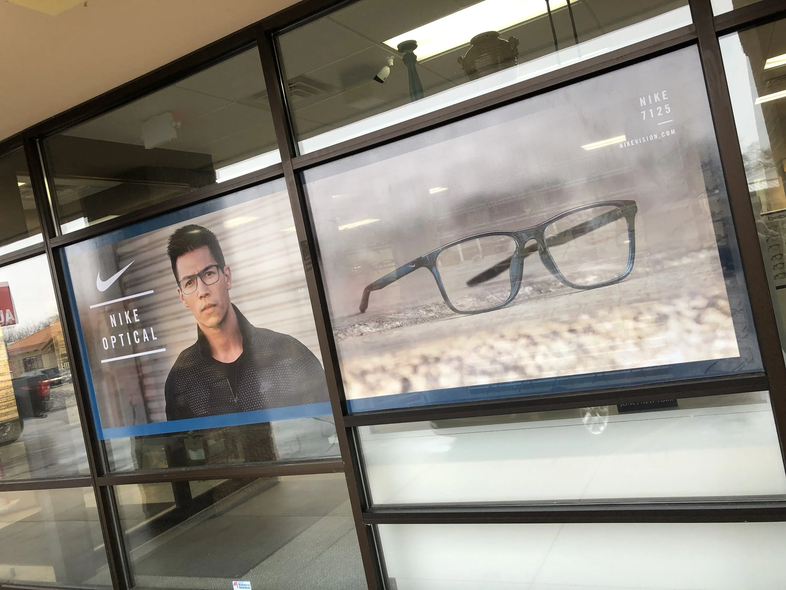 Advertisement for Nike optical glasses featuring a man with dark hair and glasses on the left, and a close-up of a pair of eyeglasses on the right.