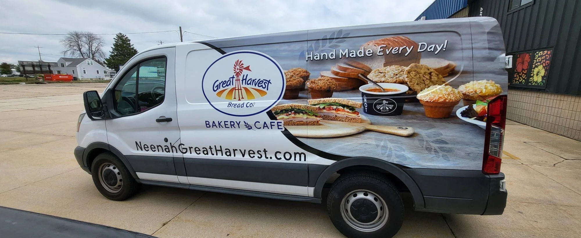 A commercial van advertising Great Harvest Bread Co. bakery cafe with images of sandwiches, baked goods, and soup, along with the text "Hand Made Every Day!" and the company's website