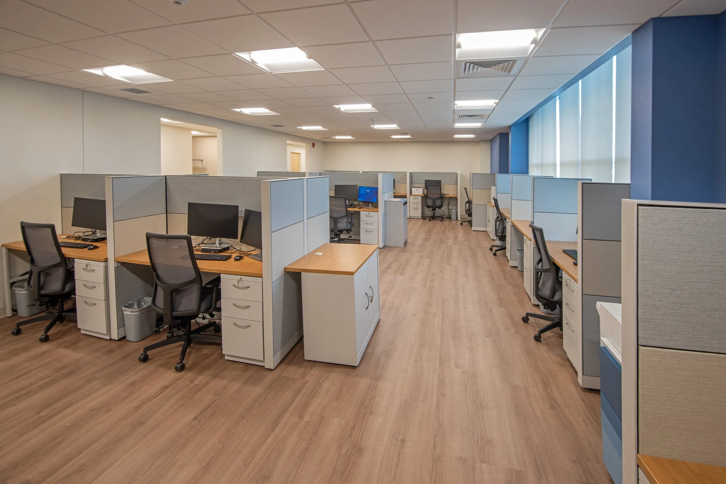 multiple small cubicles with desks, chairs, and computers for clinicians
