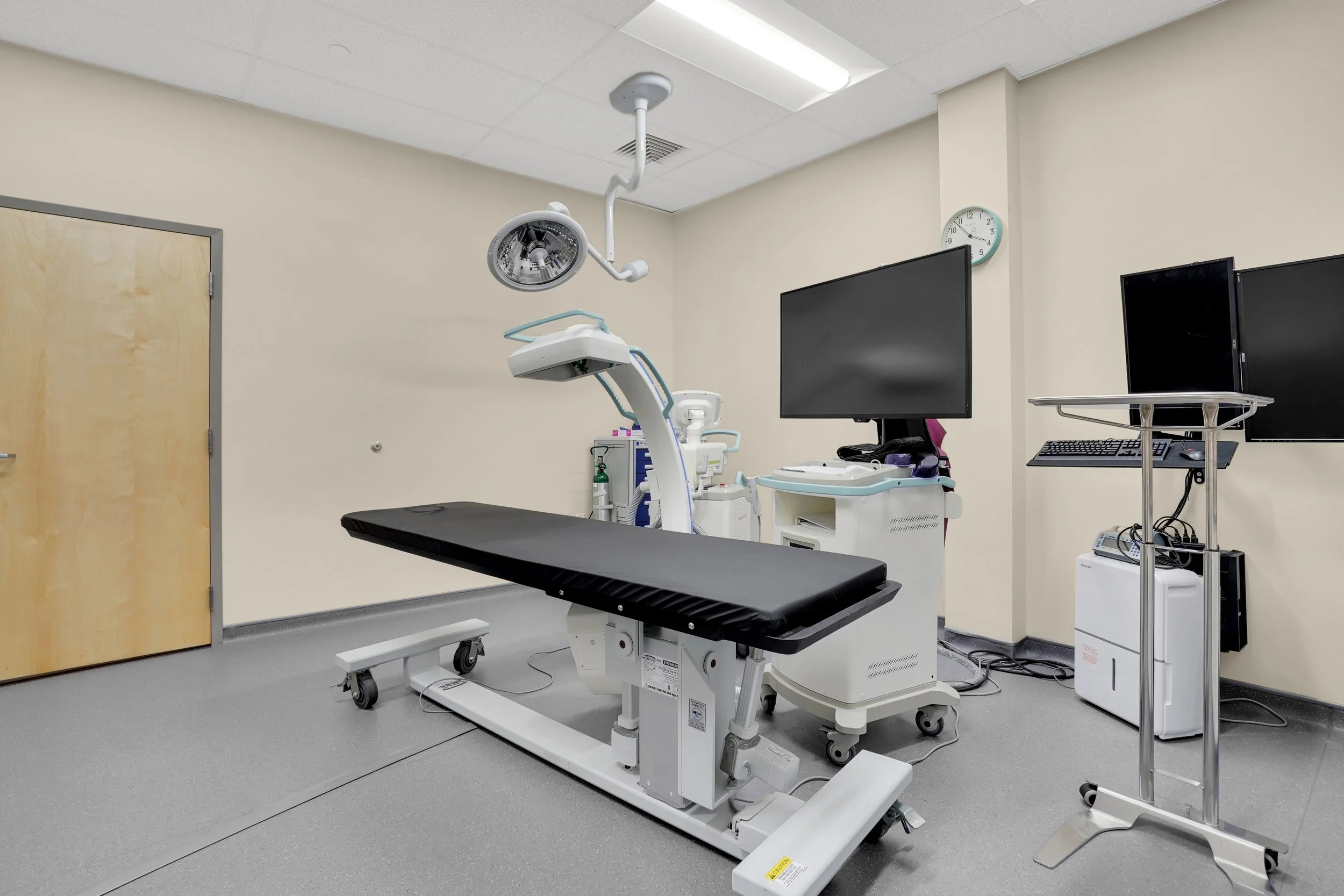 surgical room with table, lights, computer screens and medical devices.