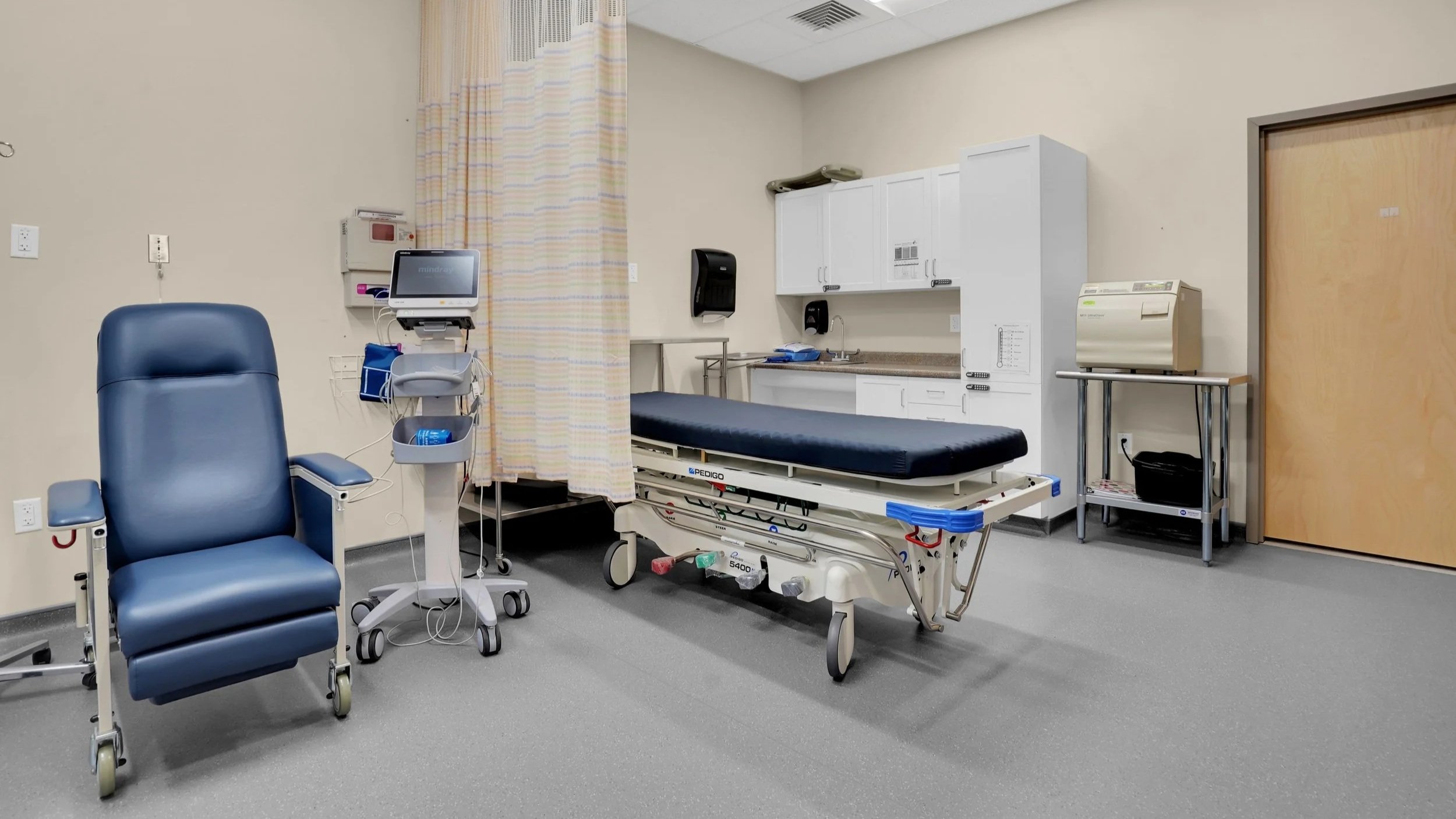 ambulatory patient room with curtain divider, gurney, patient chair, and medical devices