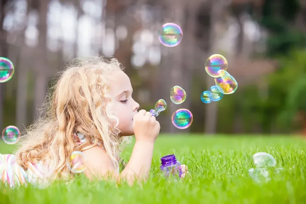 colorful, floating bubbles surround her against a soft, out-of-focus background of trees.