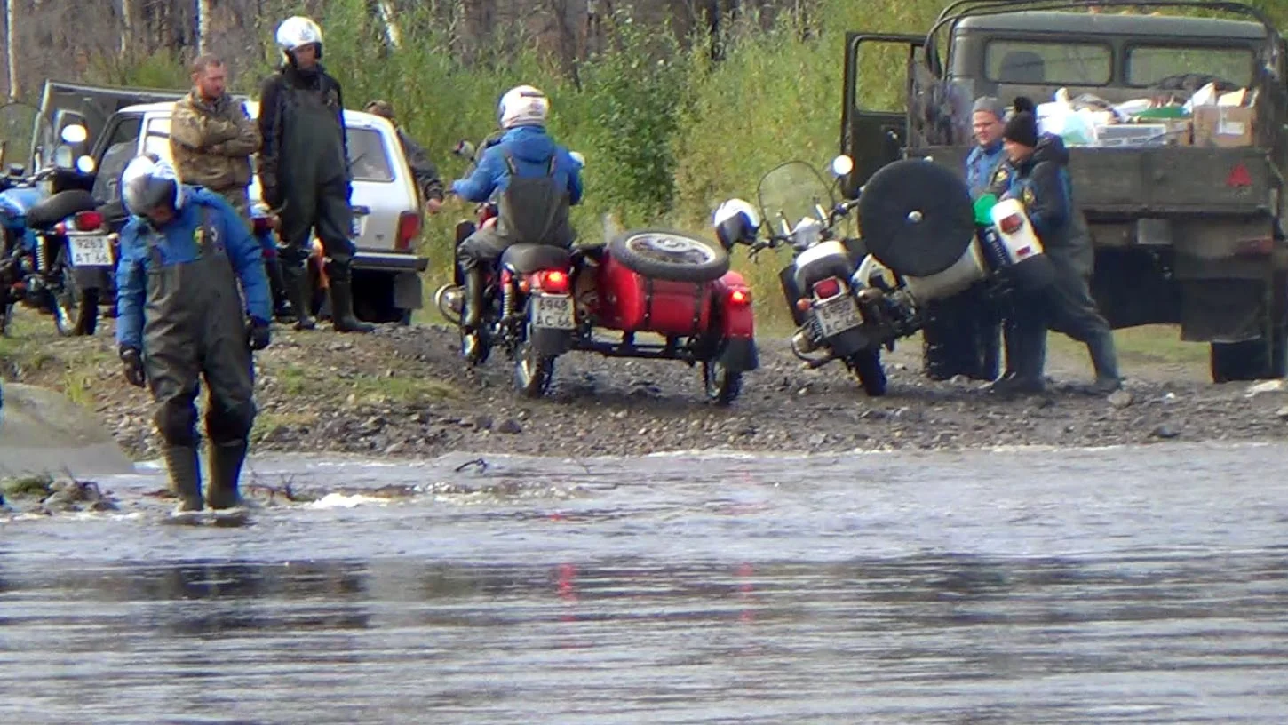 After a deep water crossing, the guys bail water out of the tub of the white Ural.