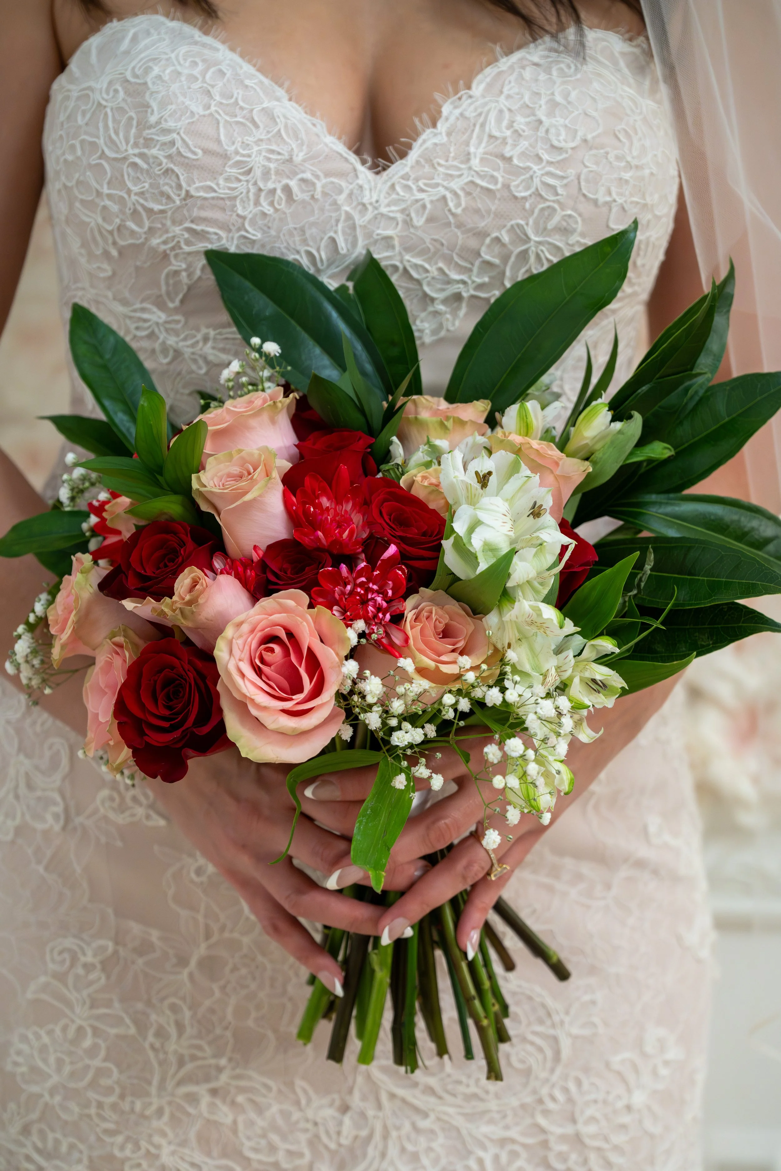 A bride holding a bouquet of pink, red, and white flowers with green leaves.