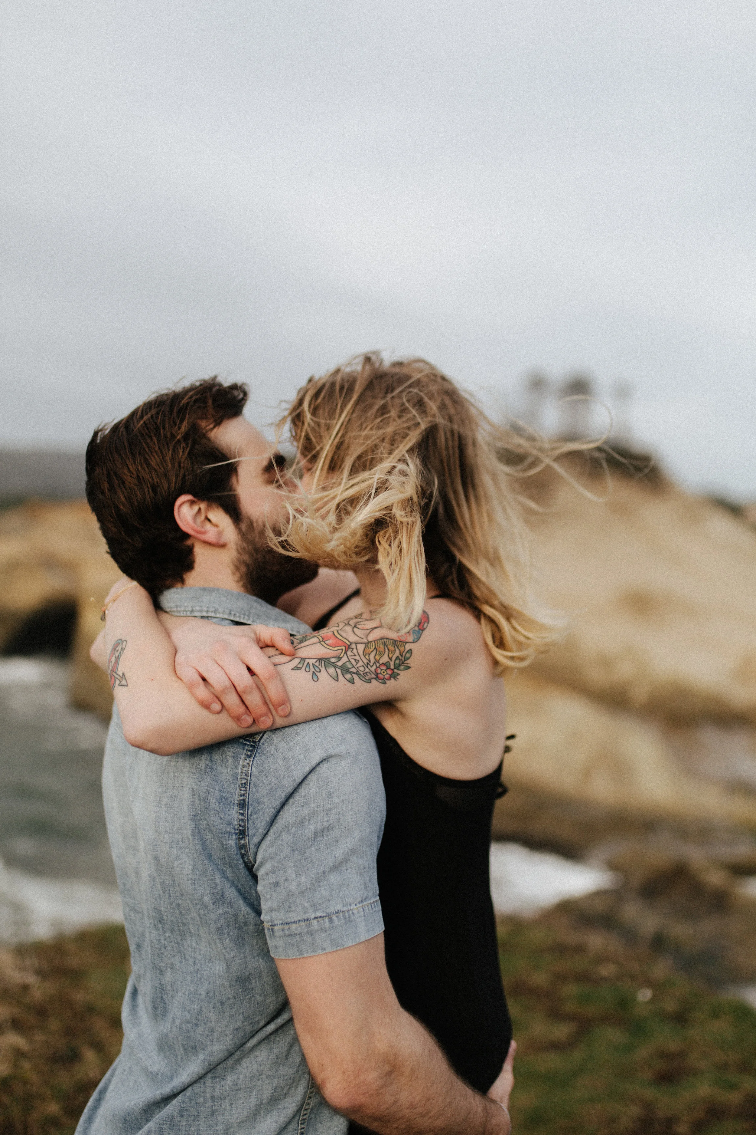  Recently I have been changing my main focal point of photography off of single subject portraits and gearing more towards couples. I do still love working one-on-one and creating something beautiful, but I love seeing the chemistry of working with couples. Last weekend I was able to stay at the coast for a few nights with friends, and ended the trip with a lovely couples shoot at Cape Kiwanda. This was the first sunny weekend in about 4 months. We have been so used to rainy days and overcast skies here in Oregon, so needless to say, the beach was very crowded. I've been to this location a number of times, so I was able to show Carly and Tyler a few hidden spots they haven't explored yet. Although it was sunny, it was still very cold and very windy. when we first got to the beach we noticed and ambulance and other search and rescue vehicles from the neighboring towns. They had evacuated all the surfers out of the water, and had two jet skis as well as a helicopter circling the water. We didn't find out until after the shoot, that someone had fallen off of their pontoon boat pretty far off the coast and could not climb back into it. He had been holding onto the side for more than thirty minutes while the coastguard planned a rescue operation and set it into action, towing a floatation device behind their jet ski and bringing him safely back to land.