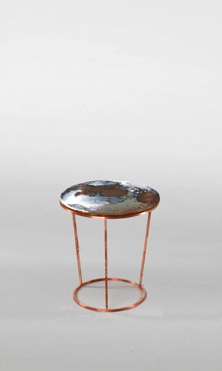 A small round side table with a metallic copper finish, featuring a reflective, textured top surface, against a plain white background.