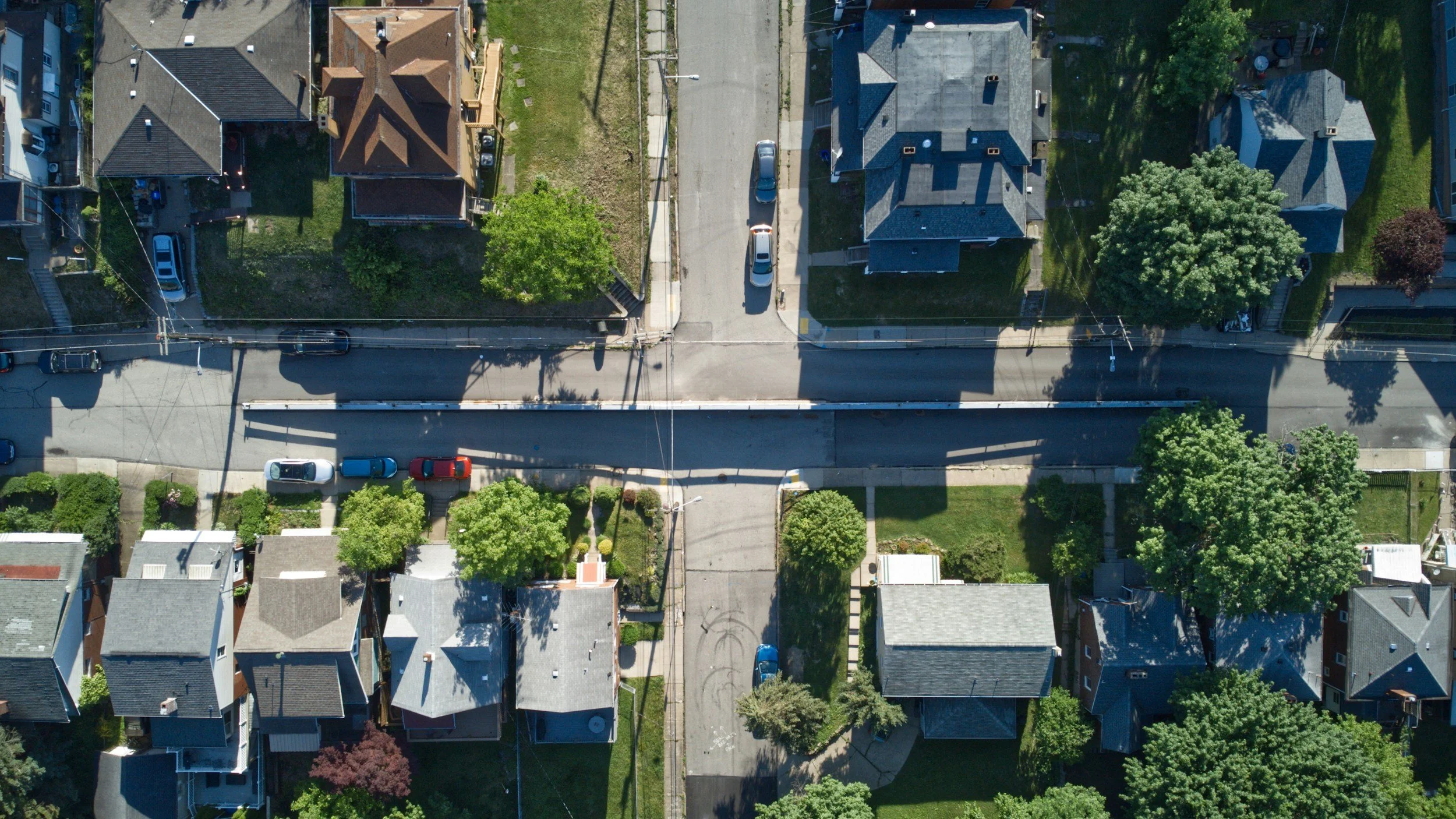 Aerial view of a residential neighborhood showing houses, streets, parked cars, trees, and gardens.