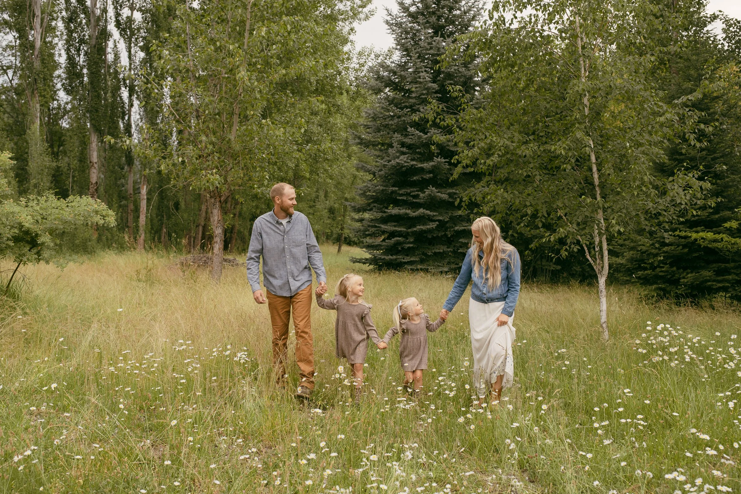 A family of four walking through a field of wild daisies during a family session in North Idaho