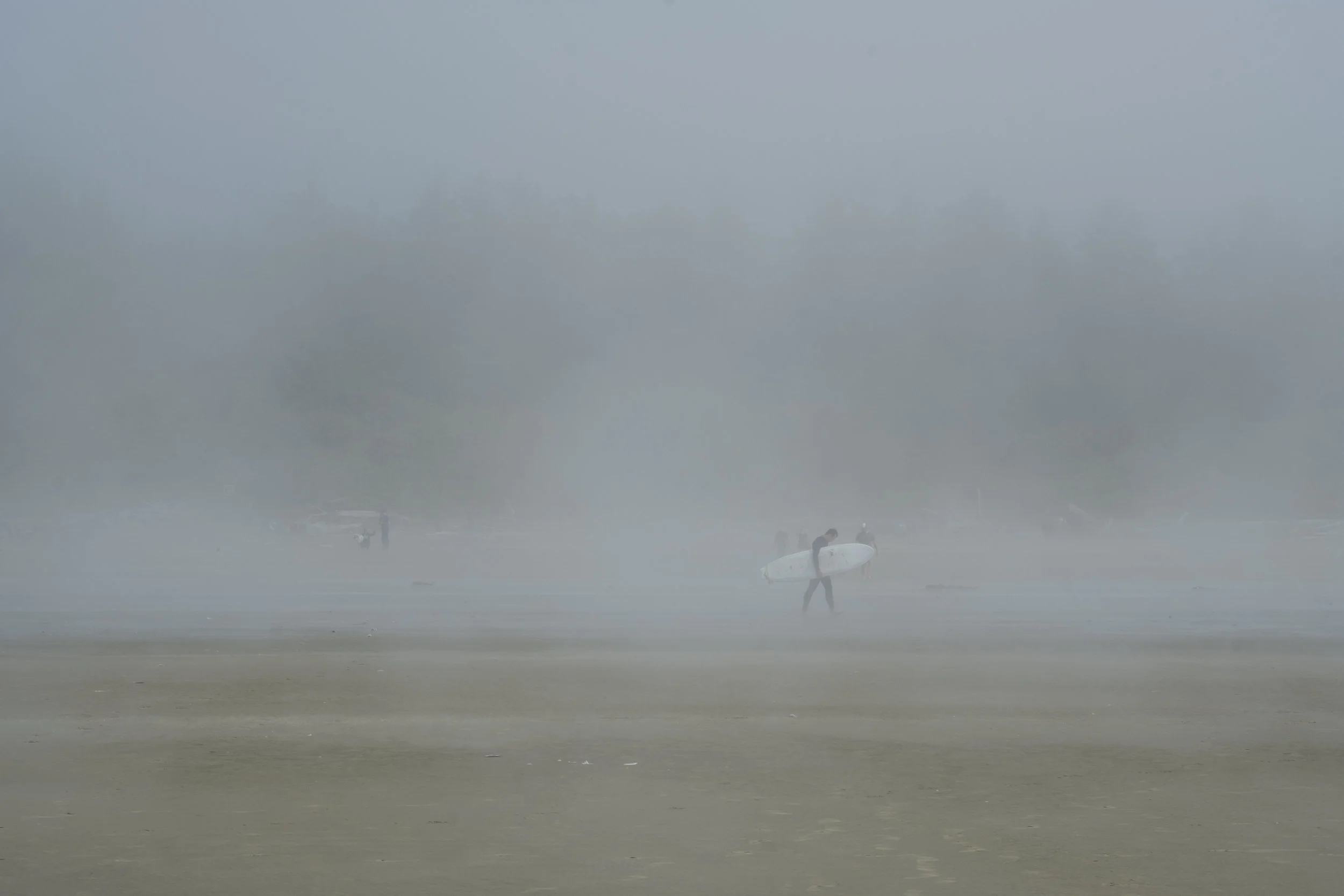 A surfer walking through a misty morning, Long Beach, Tofino
